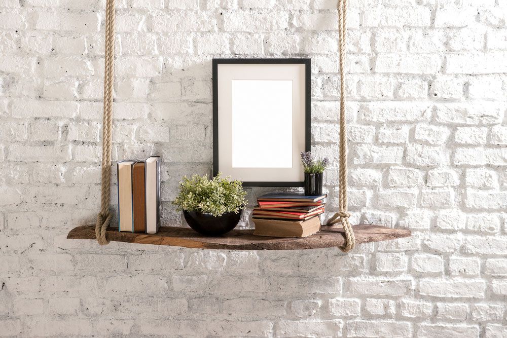 A Wooden Shelf with Books, a Picture Frame ,and a Potted Plant Hanging on A White Brick Wall — The Framer In Forster, NSW