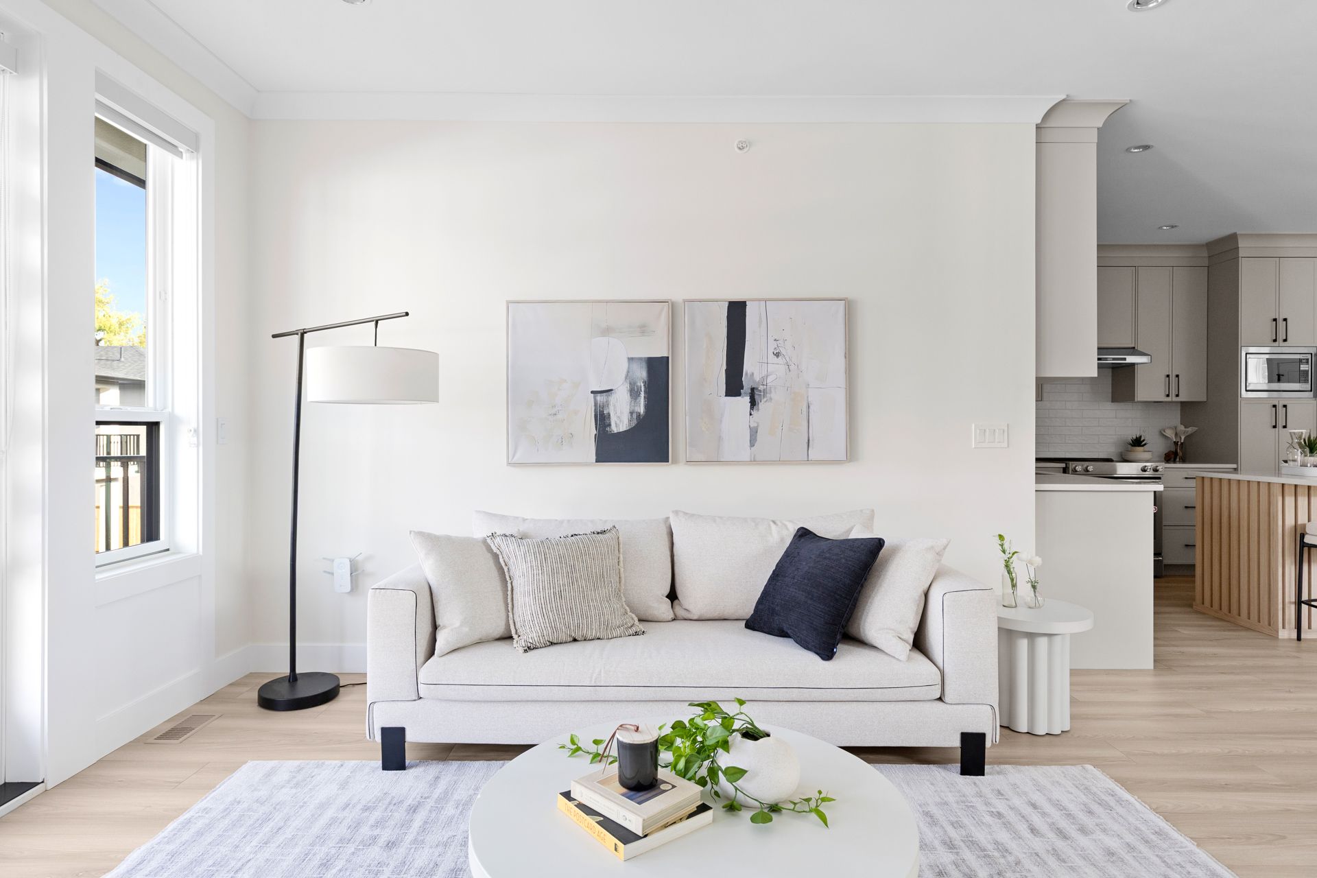 Bright modern living room with white sofa, floor lamp, abstract wall art, and coffee table