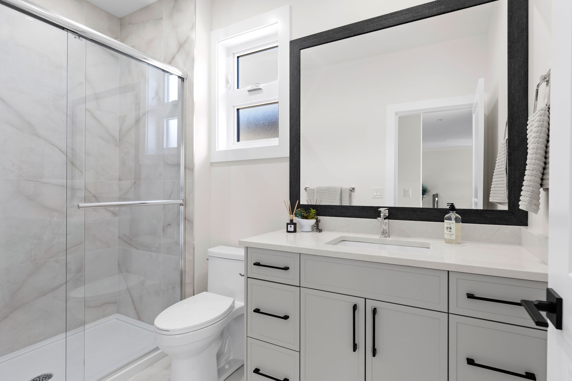 Modern white bathroom with glass shower, toilet, and gray vanity with large mirror