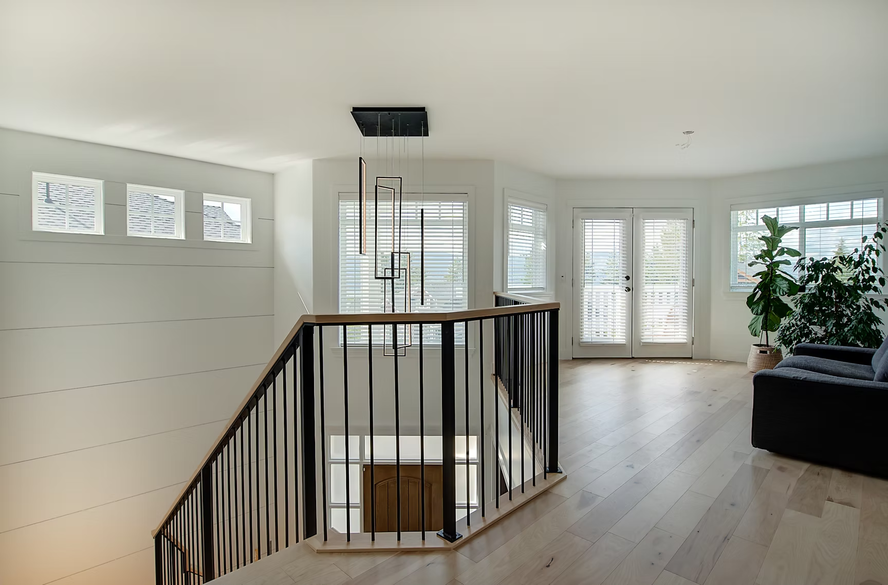 Bright modern stair landing with black railing, white walls, wood floors, and large windows.