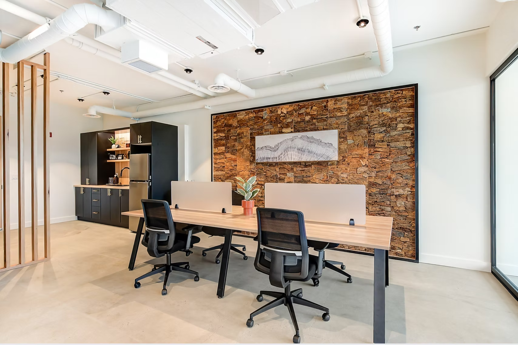 Modern office conference room with desks, black chairs, exposed ceiling, and brick accent wall