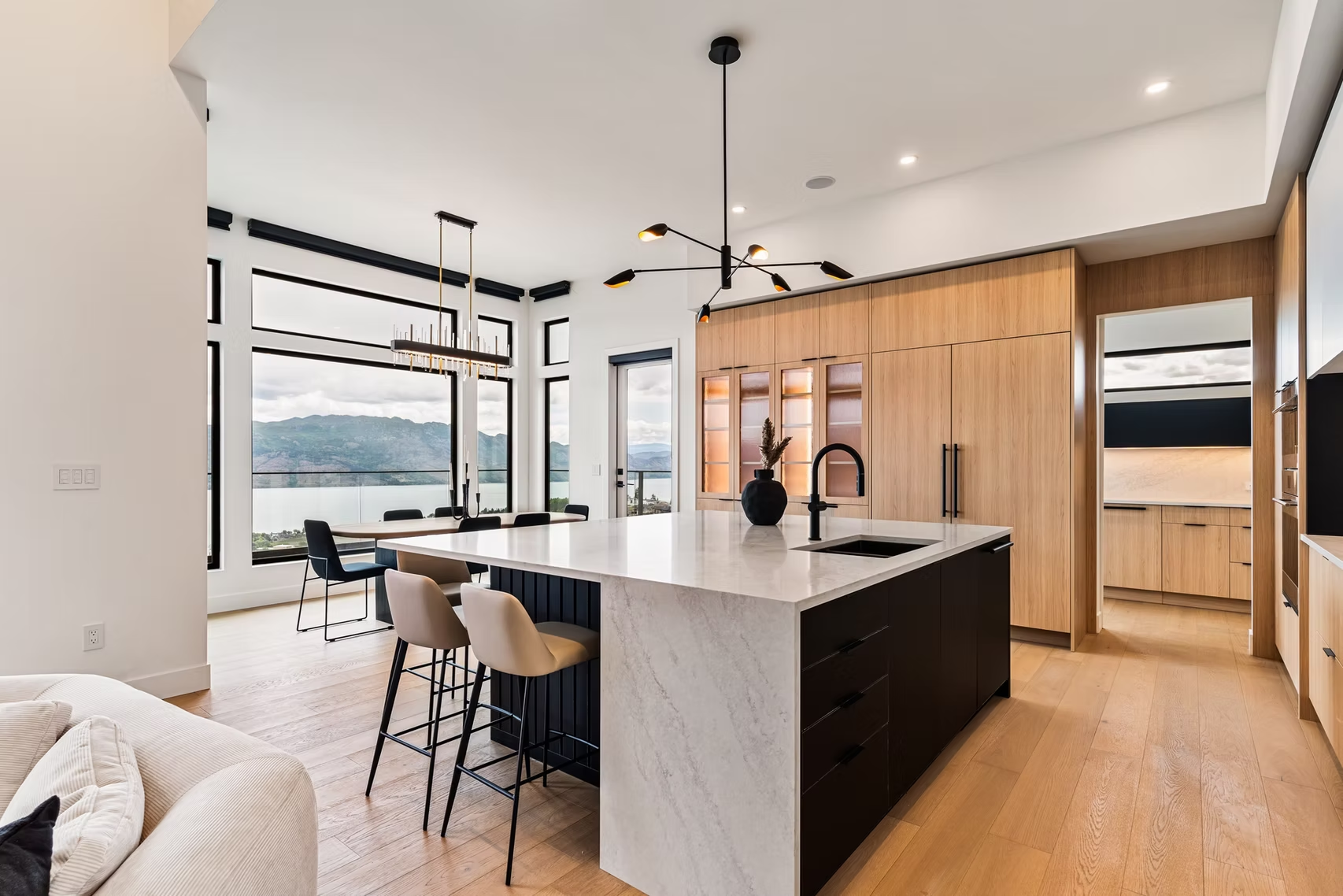 Modern kitchen with island, wood cabinets, black pendants, and large windows overlooking water