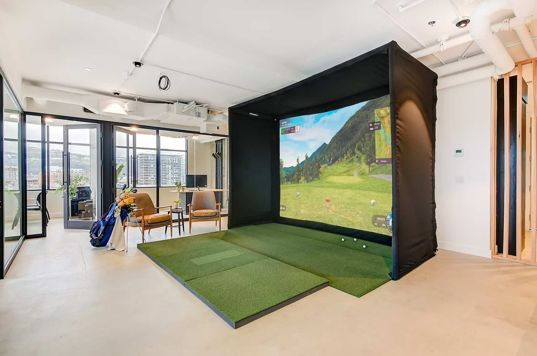 Indoor golf simulator with a large screen and green turf in a modern room