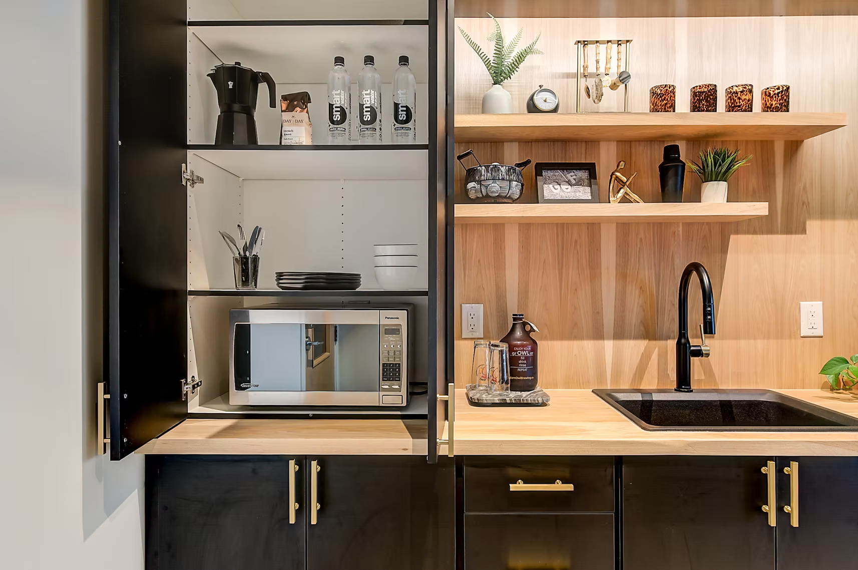 Modern kitchen with open shelves, microwave, coffee maker, sink, and black-and-wood cabinetry