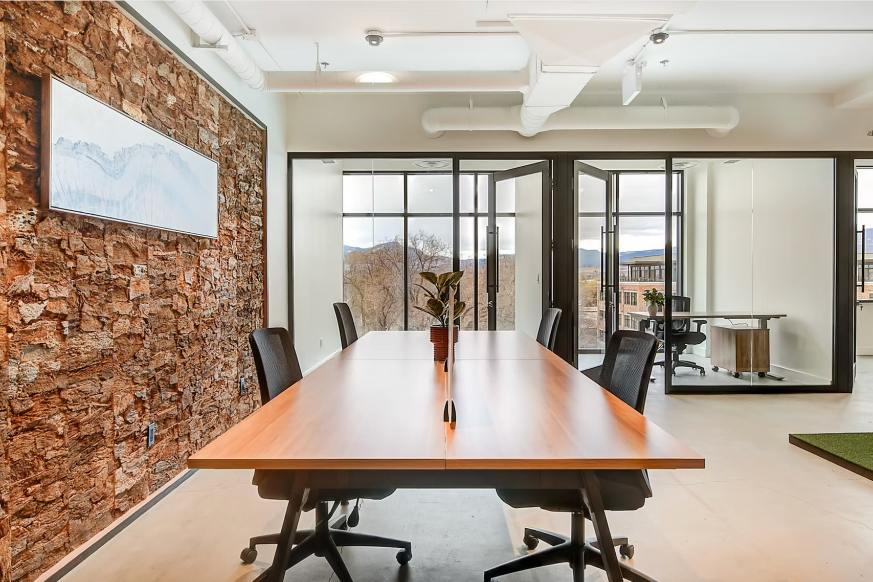 Modern conference room with long wooden table, black chairs, glass walls, and a textured copper accent wall
