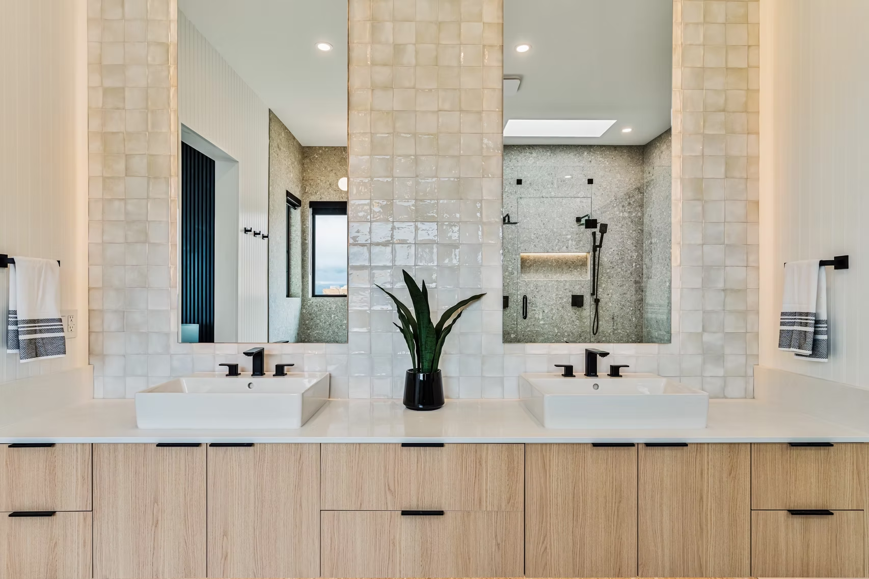 Modern double bathroom vanity with white sinks, light wood cabinets, and large mirror in a bright tiled bathroom