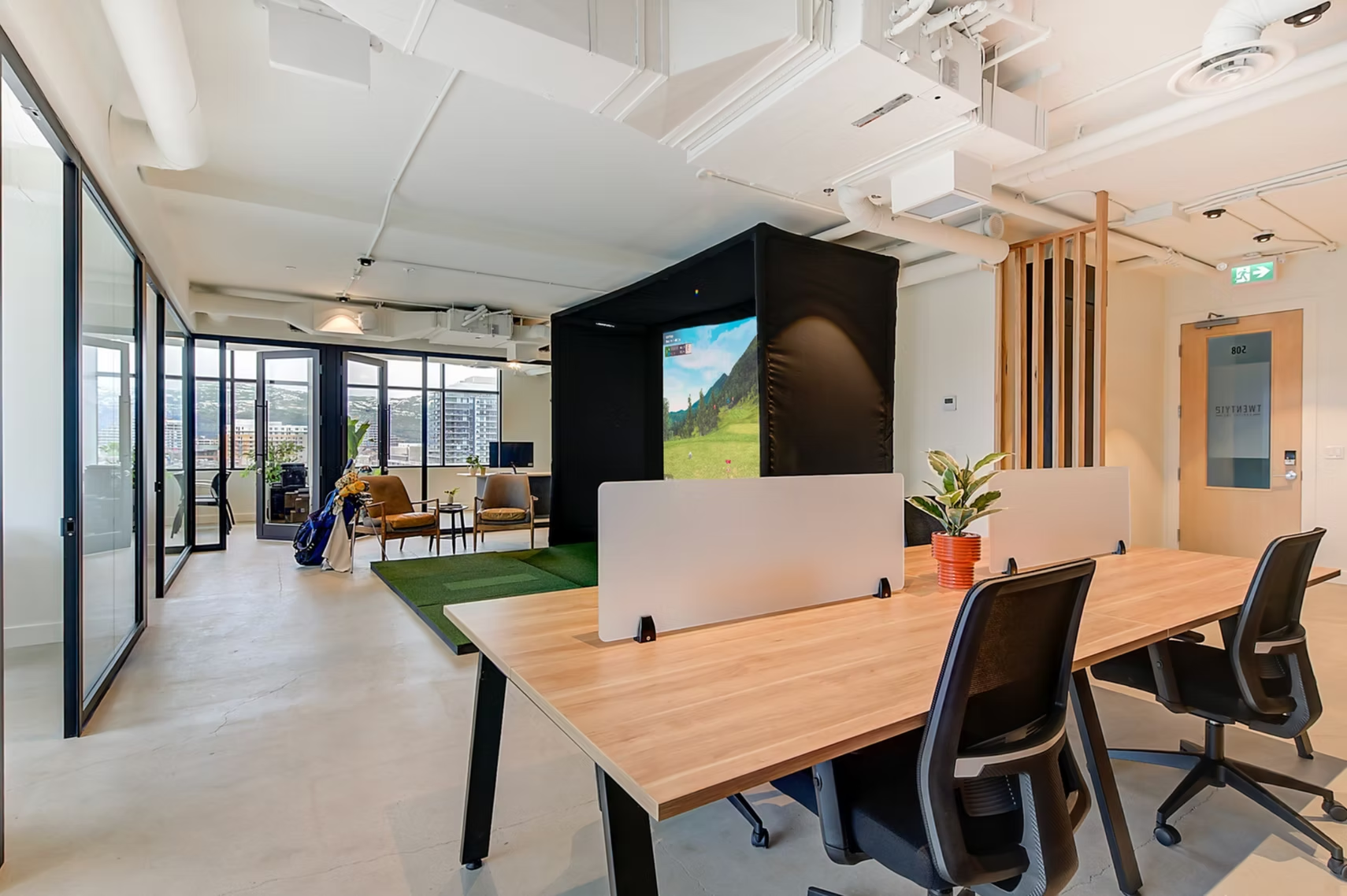 Modern office lounge with desks, chairs, glass walls, and a green indoor seating area