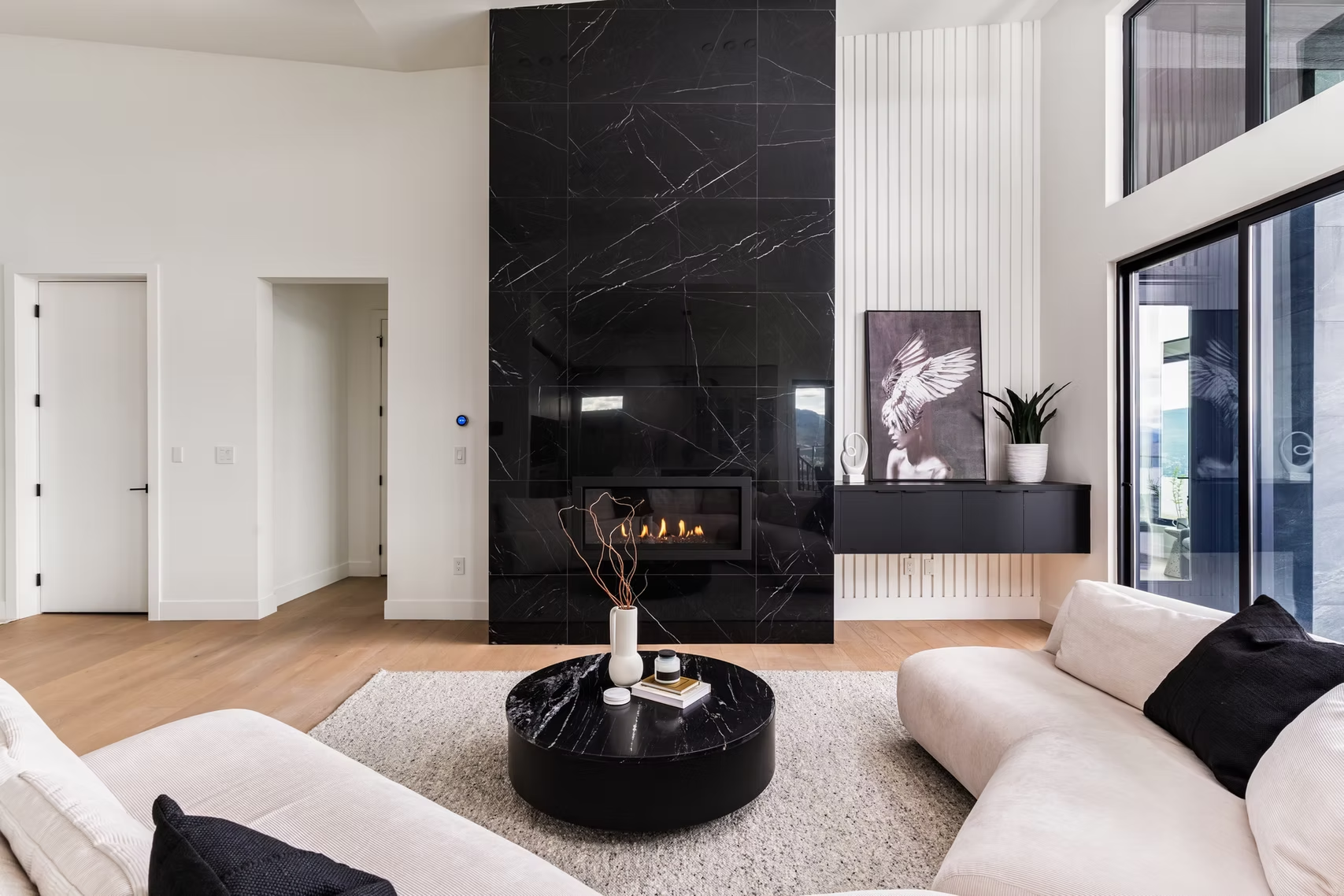 Modern living room with black fireplace wall, white sofas, and large windows overlooking a balcony.
