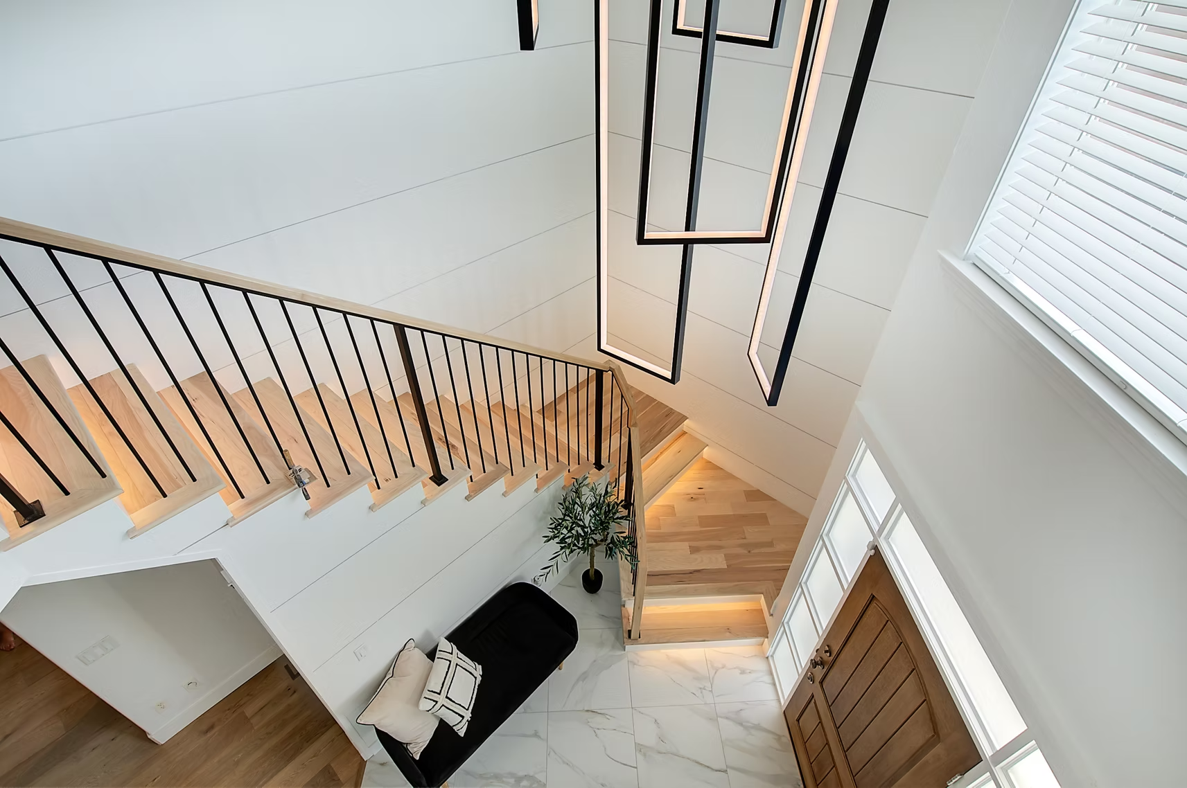 Modern stairwell with wooden steps, black railing, white walls, and a small seating area below