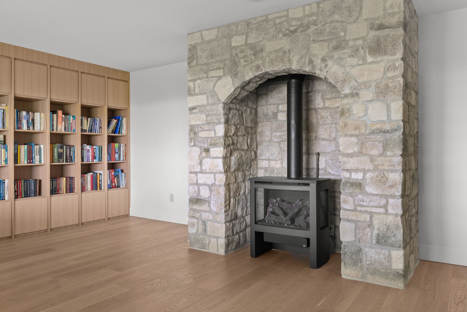 Living room with stone fireplace, wood stove, and built-in bookshelves along the wall