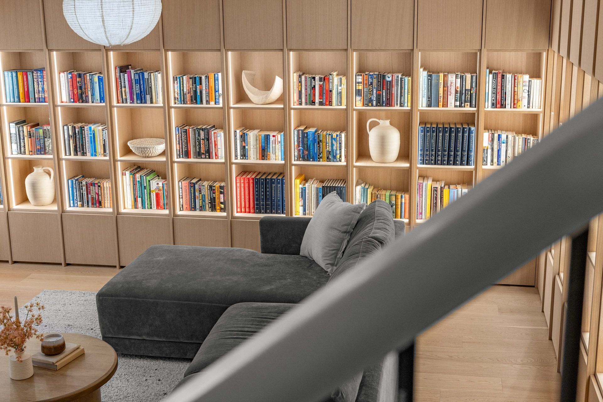 Cozy living room with a gray sofa, round table, and a wall of bookshelves lined with books and decor