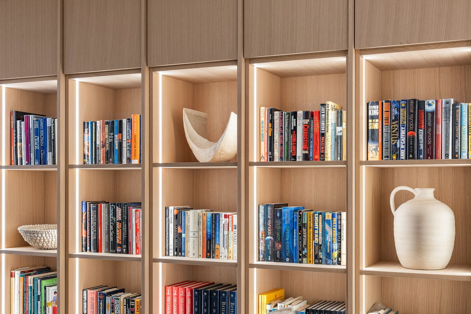 Wooden bookshelf with neatly arranged colorful books and decorative vases in a warm interior.