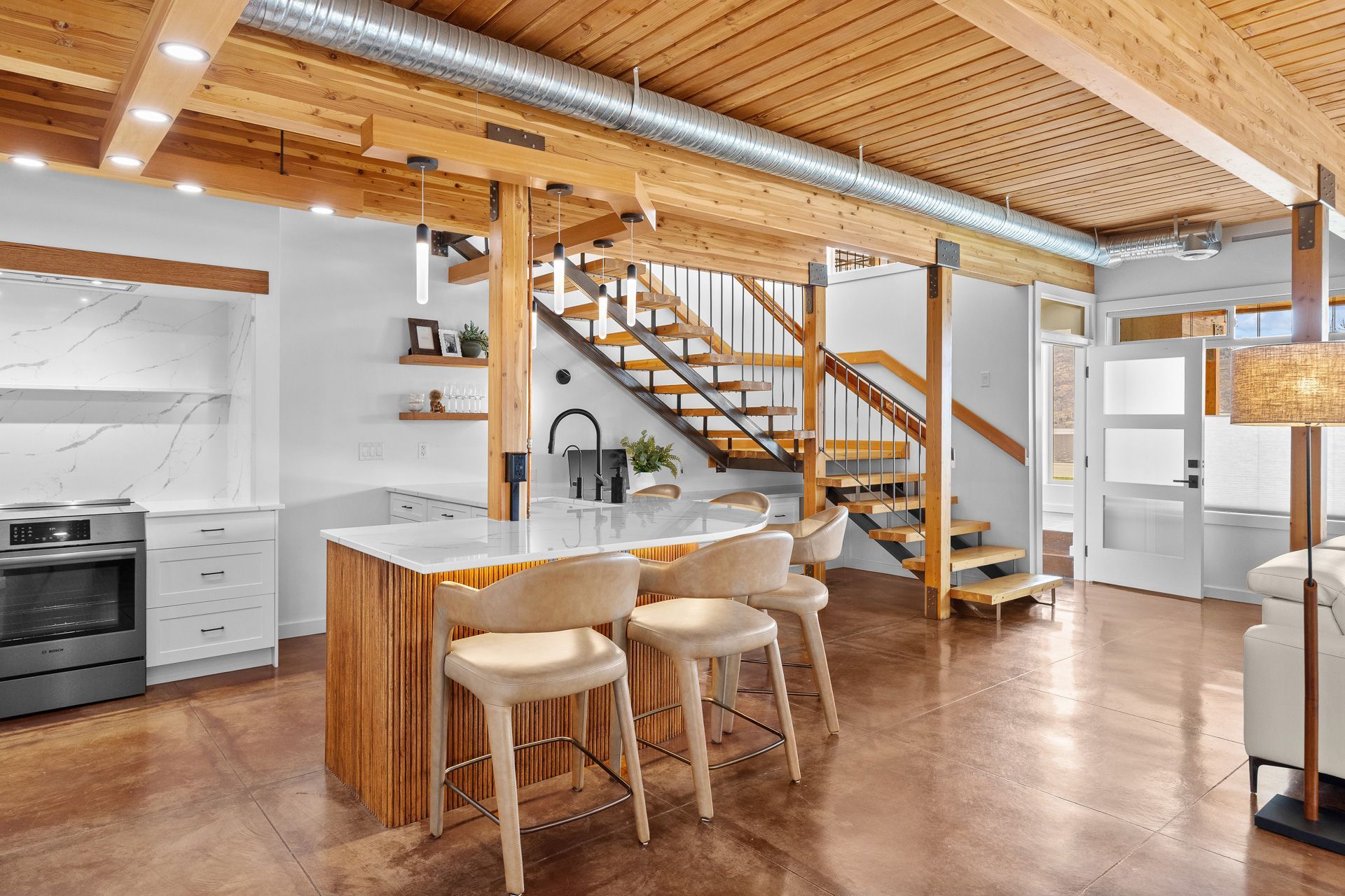 Modern kitchen with wood ceiling, island counter, and staircase to a loft.