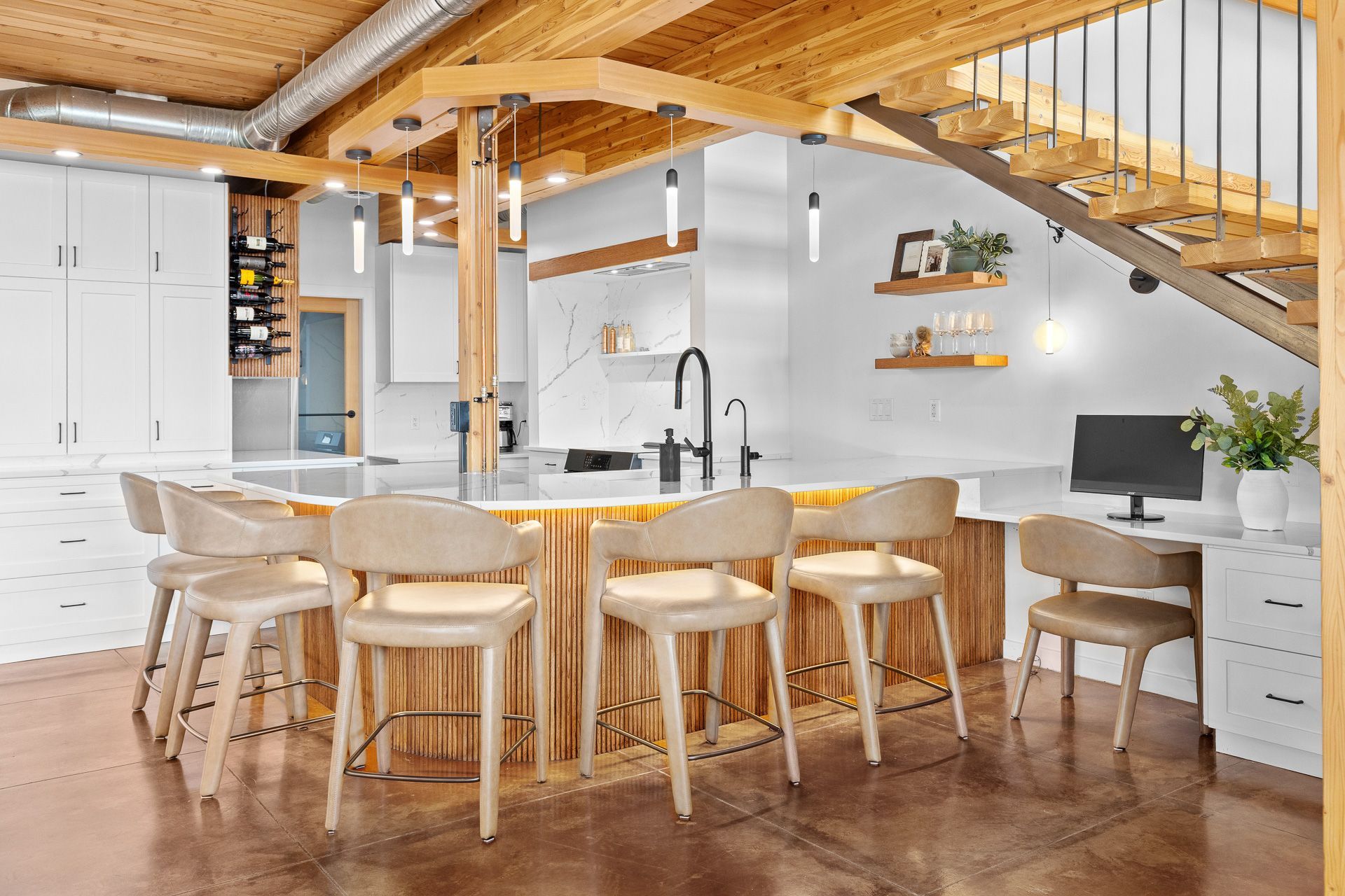 Bright modern kitchen with wood accents, white island stools, and a staircase above.