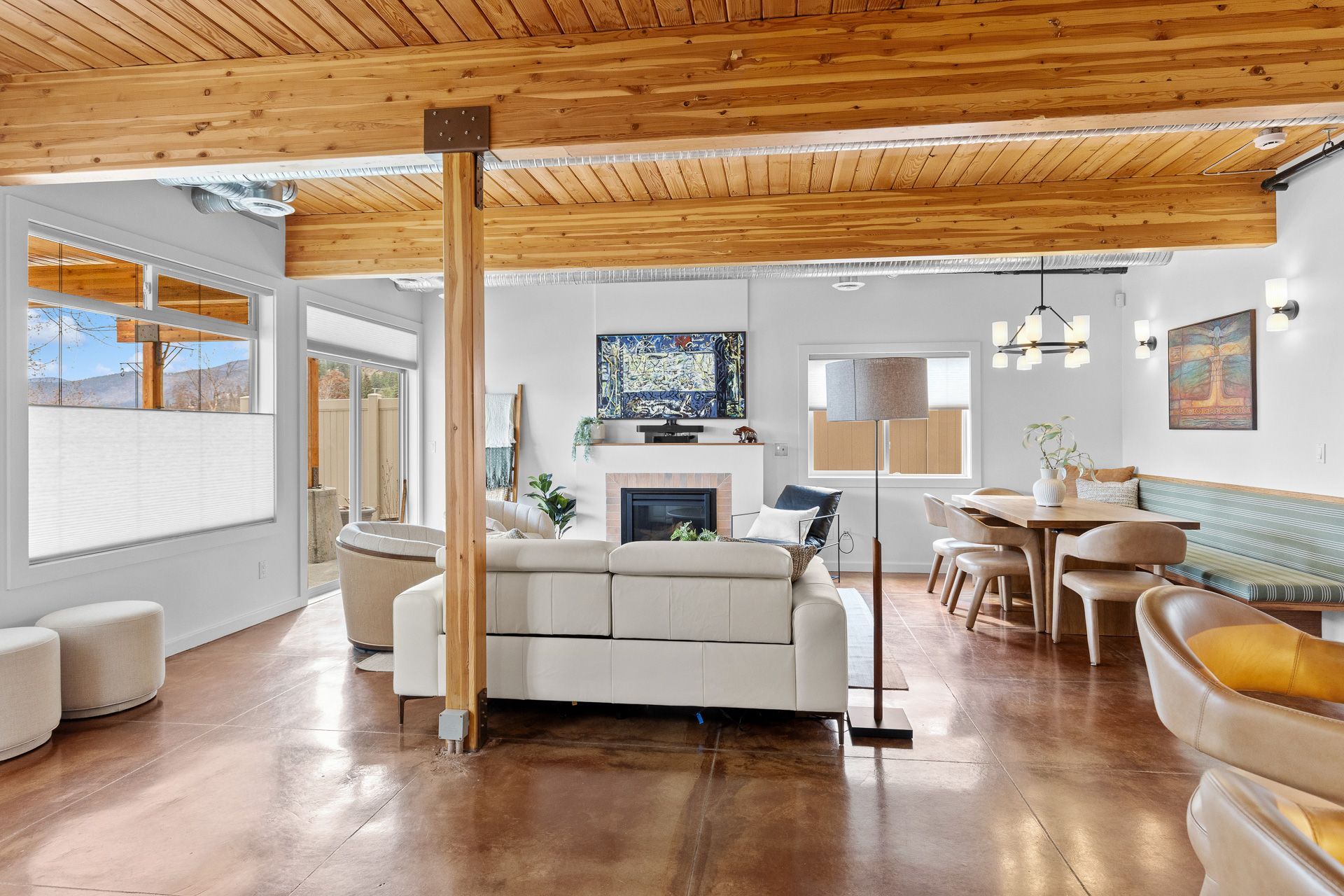 Open-plan living room with wood ceiling, white sofas, fireplace, and dining area with large windows