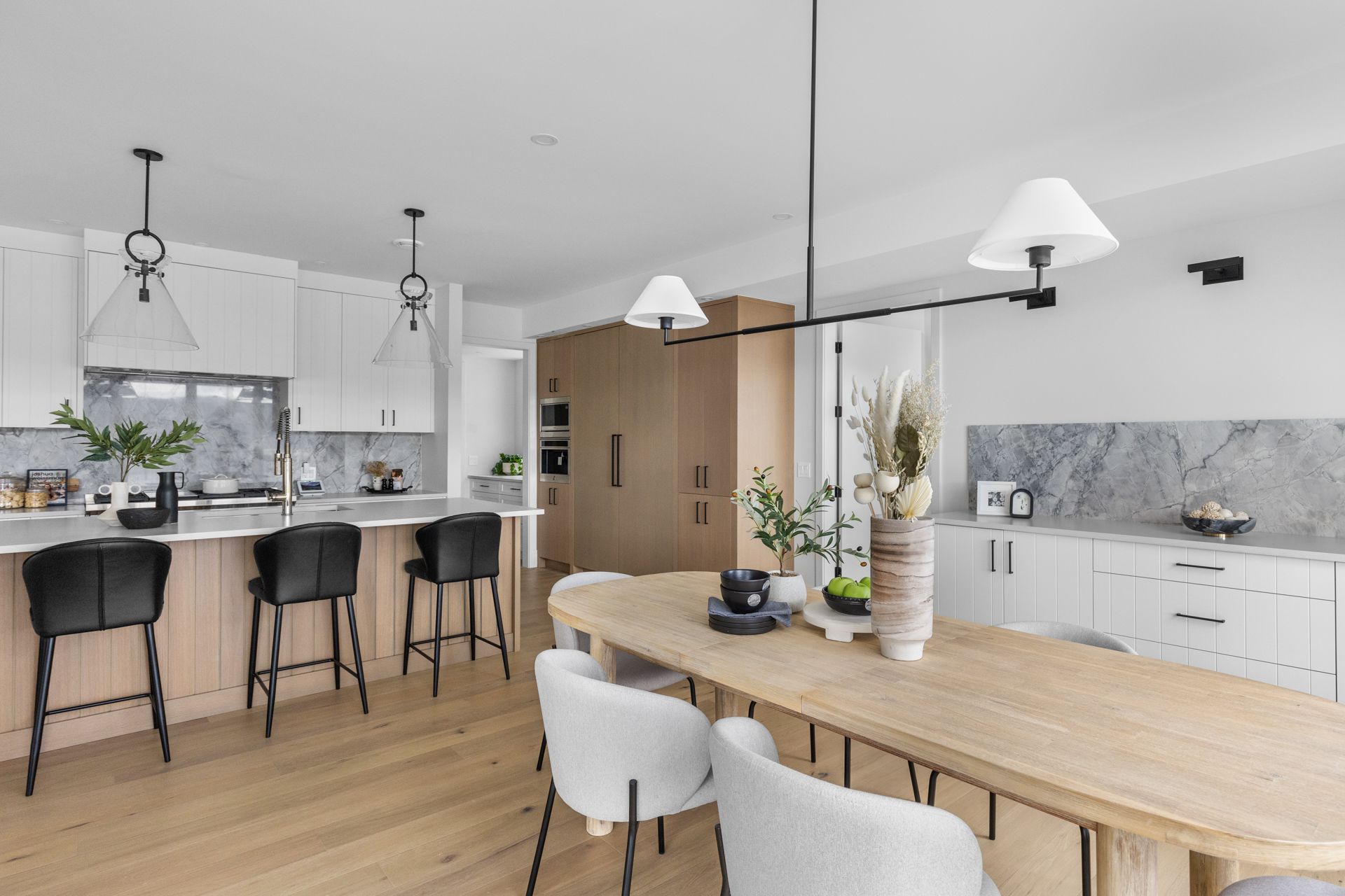 Bright modern kitchen and dining area with wood table, bar stools, and white cabinets