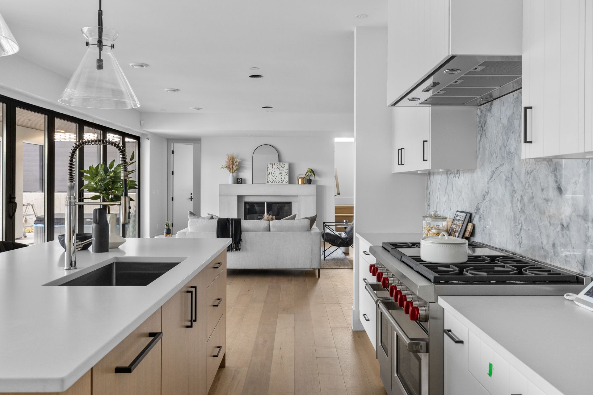 Bright modern kitchen with white cabinets, marble island, and open living area with large windows