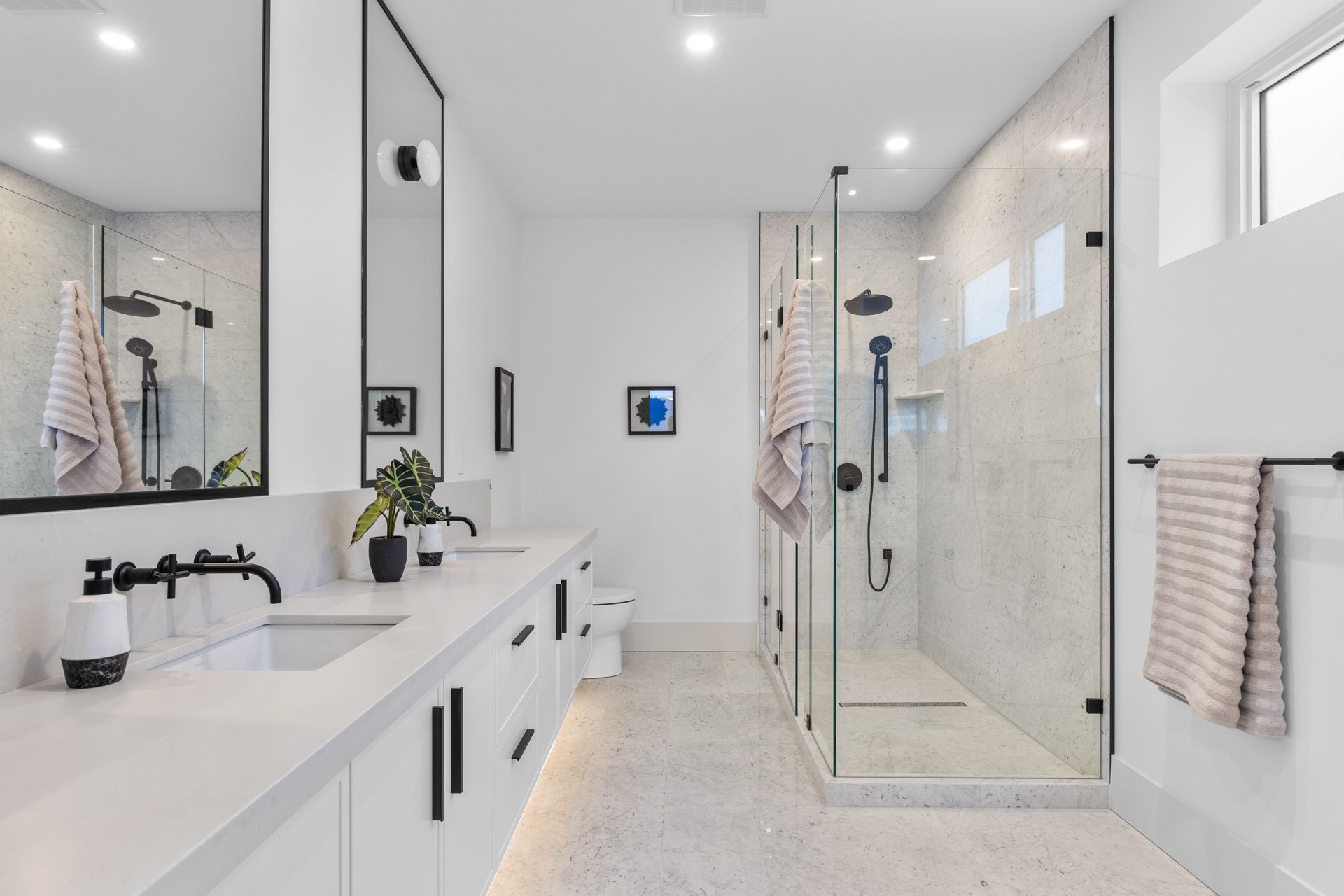 Bright modern bathroom with white vanity, glass shower, and striped towels