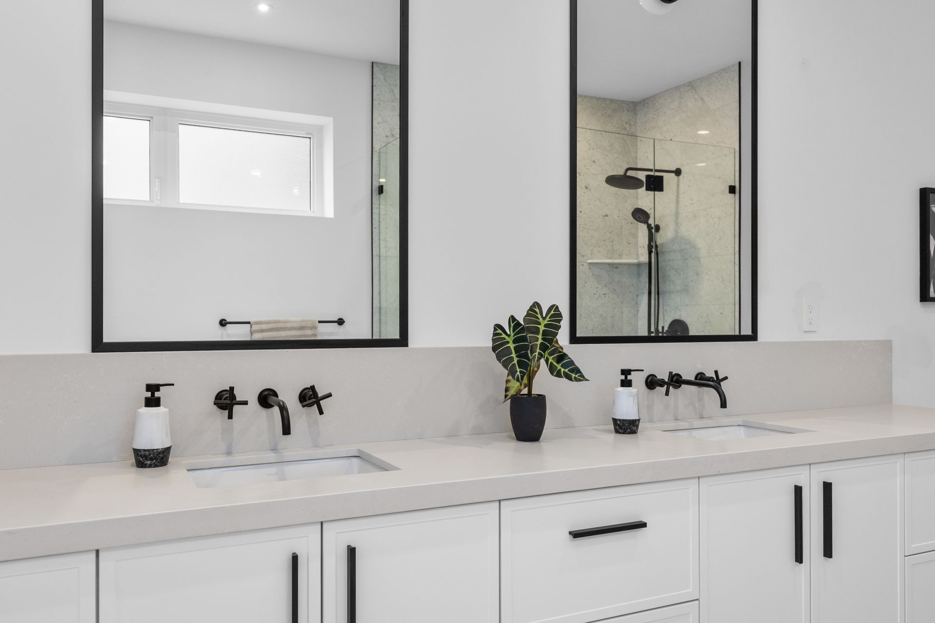 Modern bathroom vanity with dual mirrors, white countertops, black fixtures, and a shower reflection