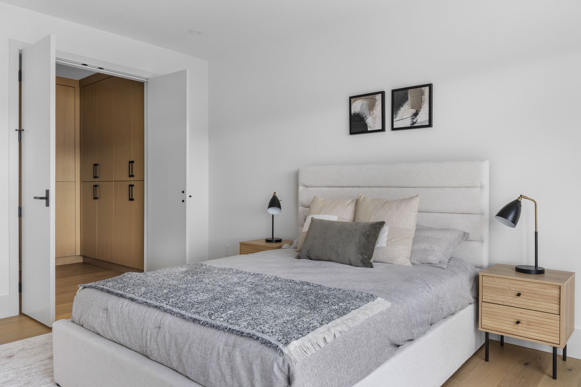 Bright minimalist bedroom with white bed, wood nightstands, black lamps, and open doorway to a hallway
