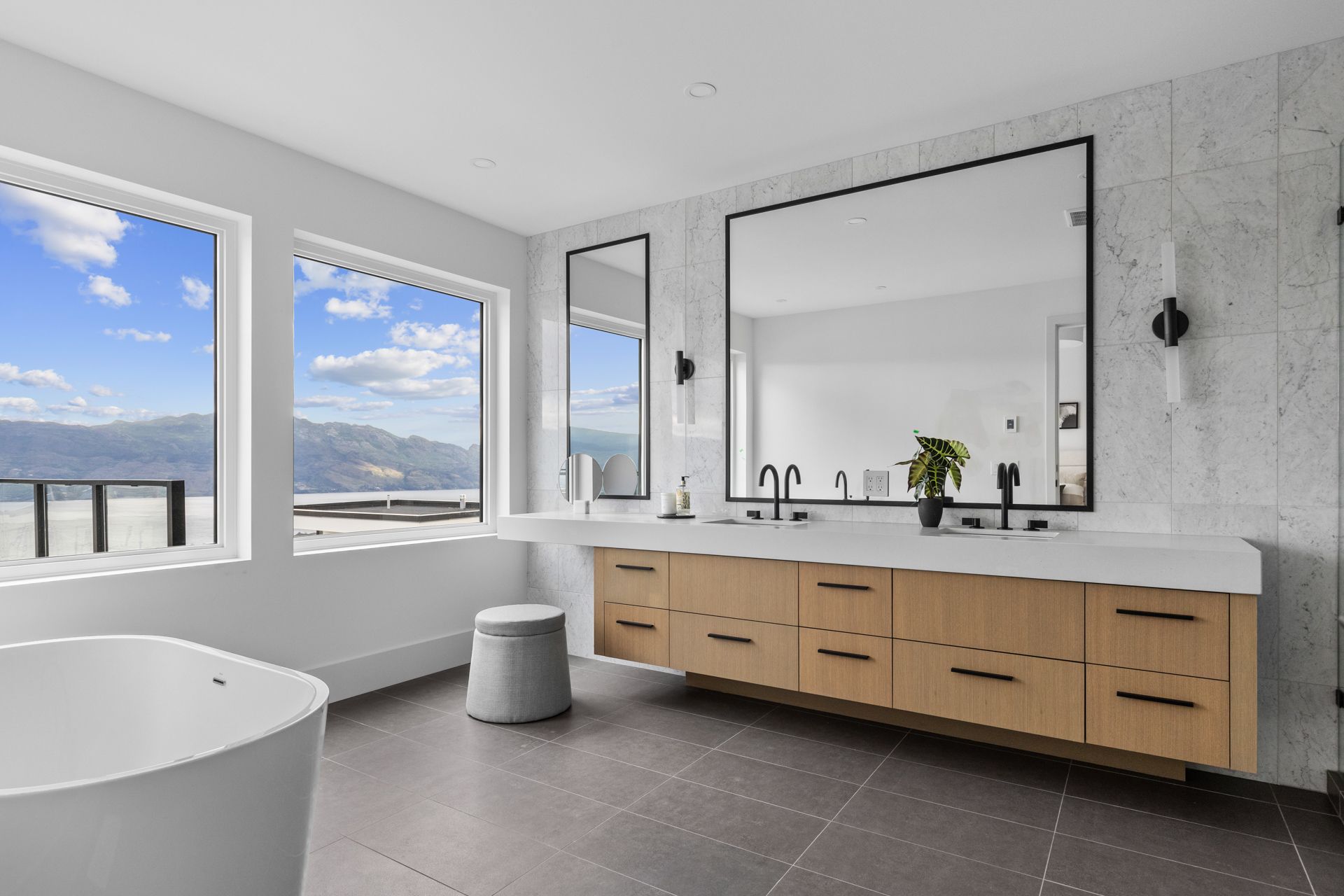 Modern bathroom with freestanding tub, wood vanity, large mirror, and mountain-view windows