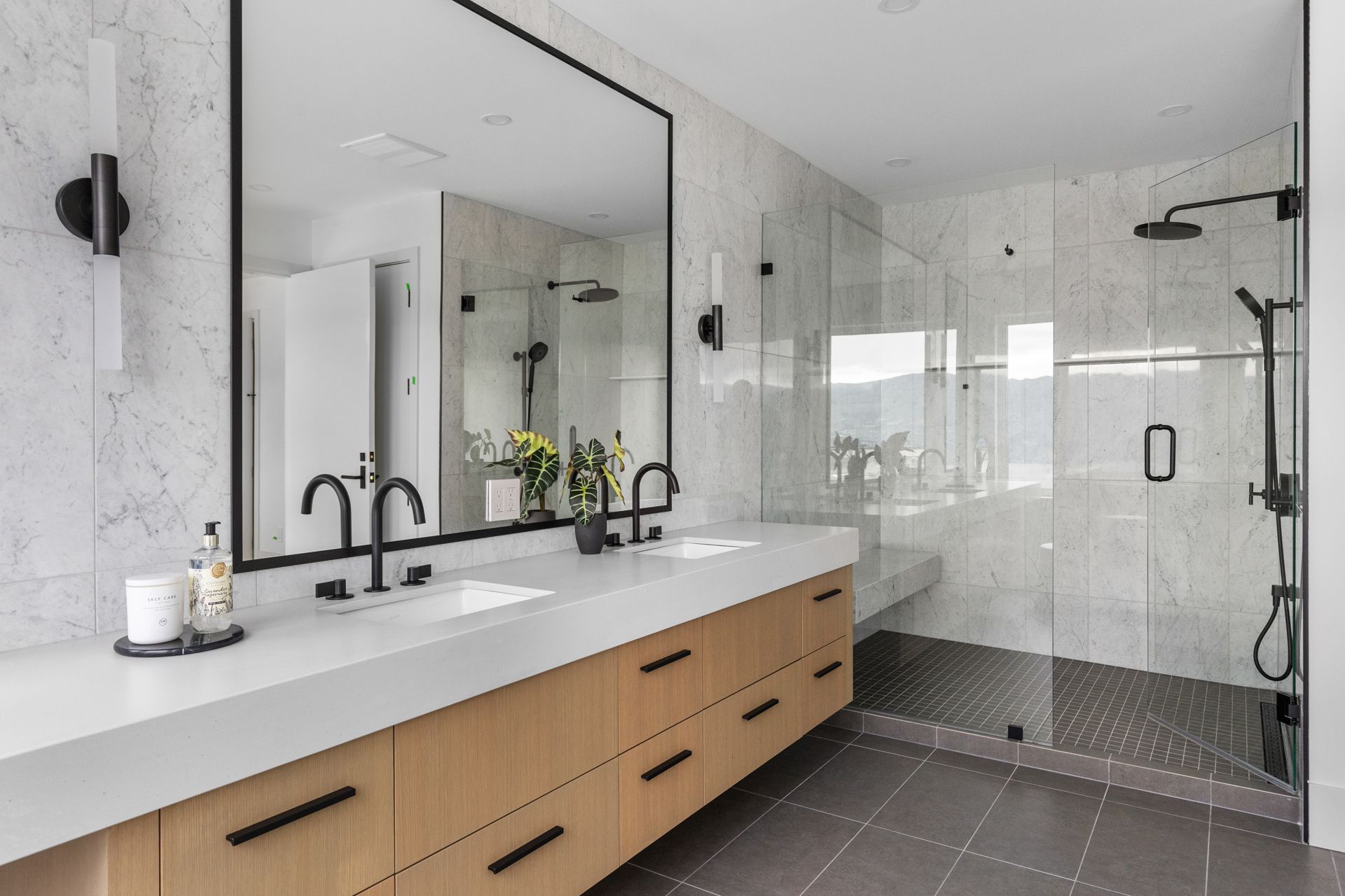 Modern bathroom with large mirror, double vanity, glass shower, and light wood cabinetry