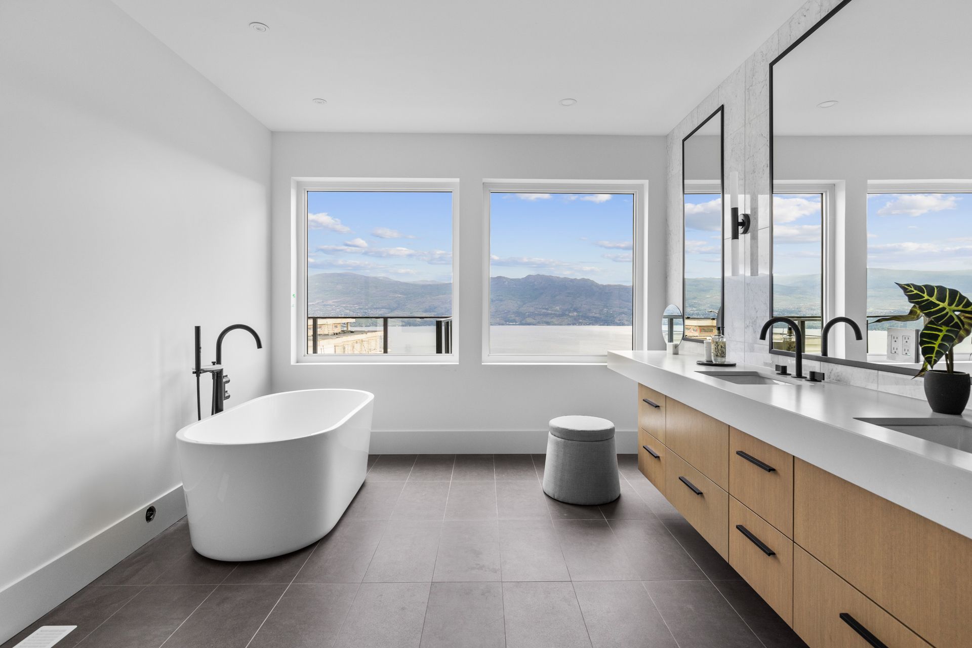 Modern white bathroom with freestanding tub, double vanity, and large windows overlooking water and mountains