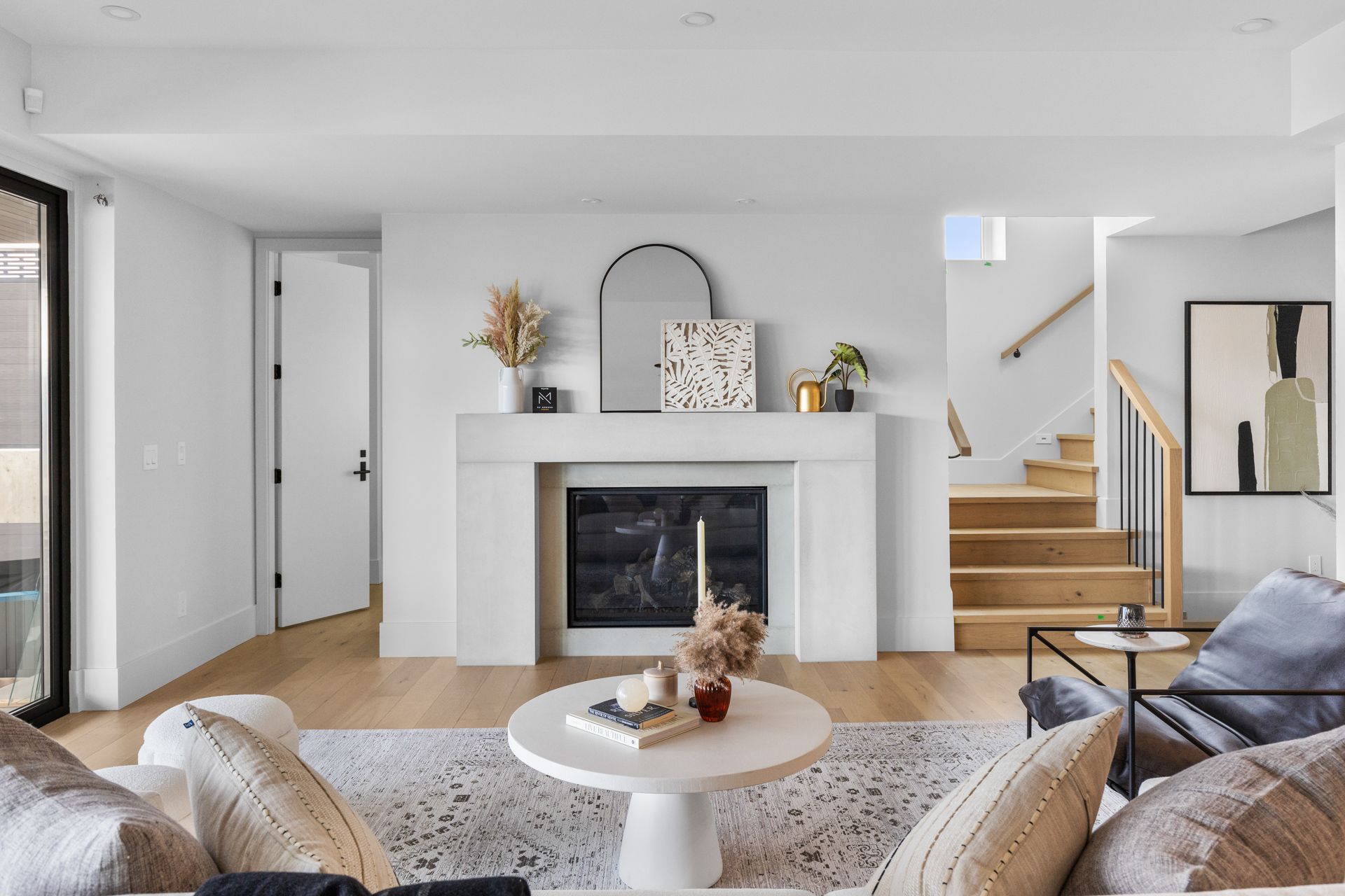 Bright living room with a white fireplace, staircase, sofa, and round coffee table.