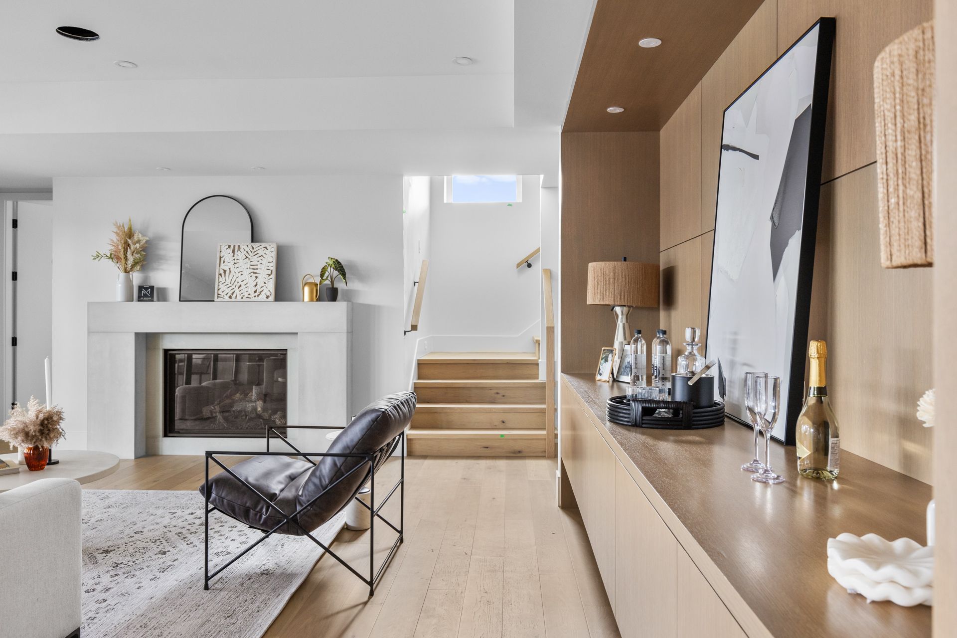 Modern living room with fireplace, floating stairs, and long wood console in a bright minimalist home