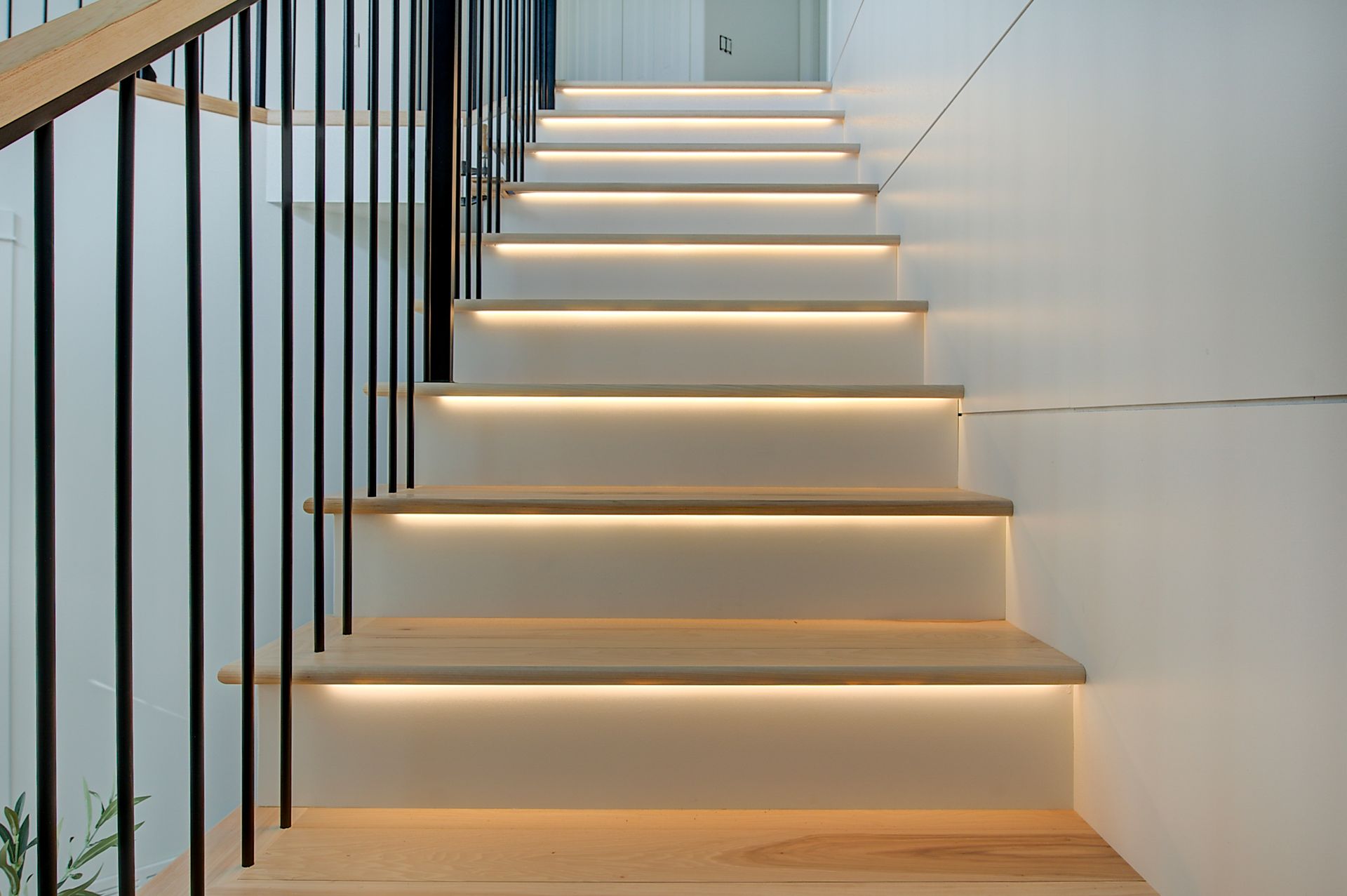 Modern indoor staircase with floating wooden steps and black railing, lit by warm strip lights