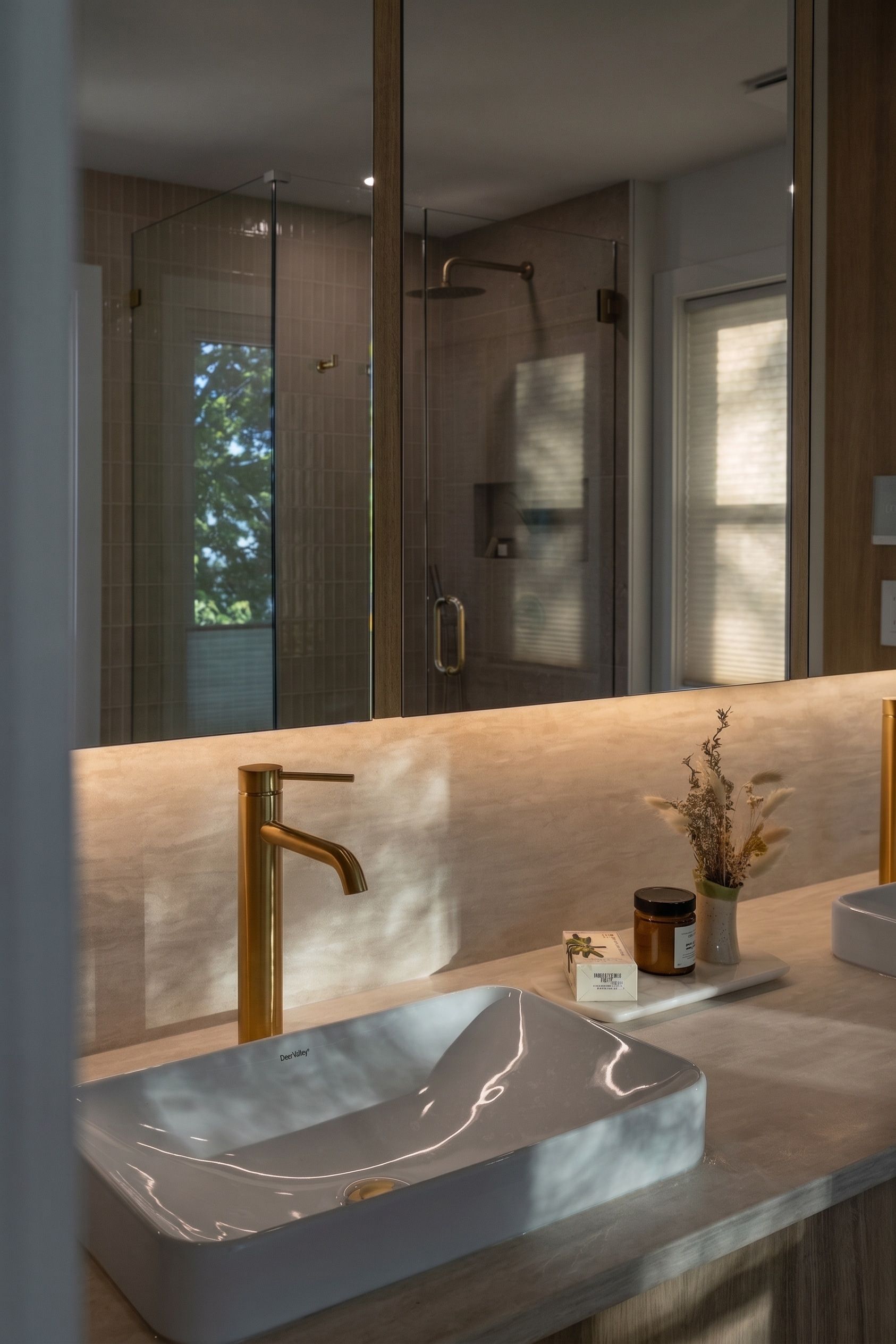 Modern bathroom vanity with vessel sink, brass faucet, and large mirror with warm backlighting