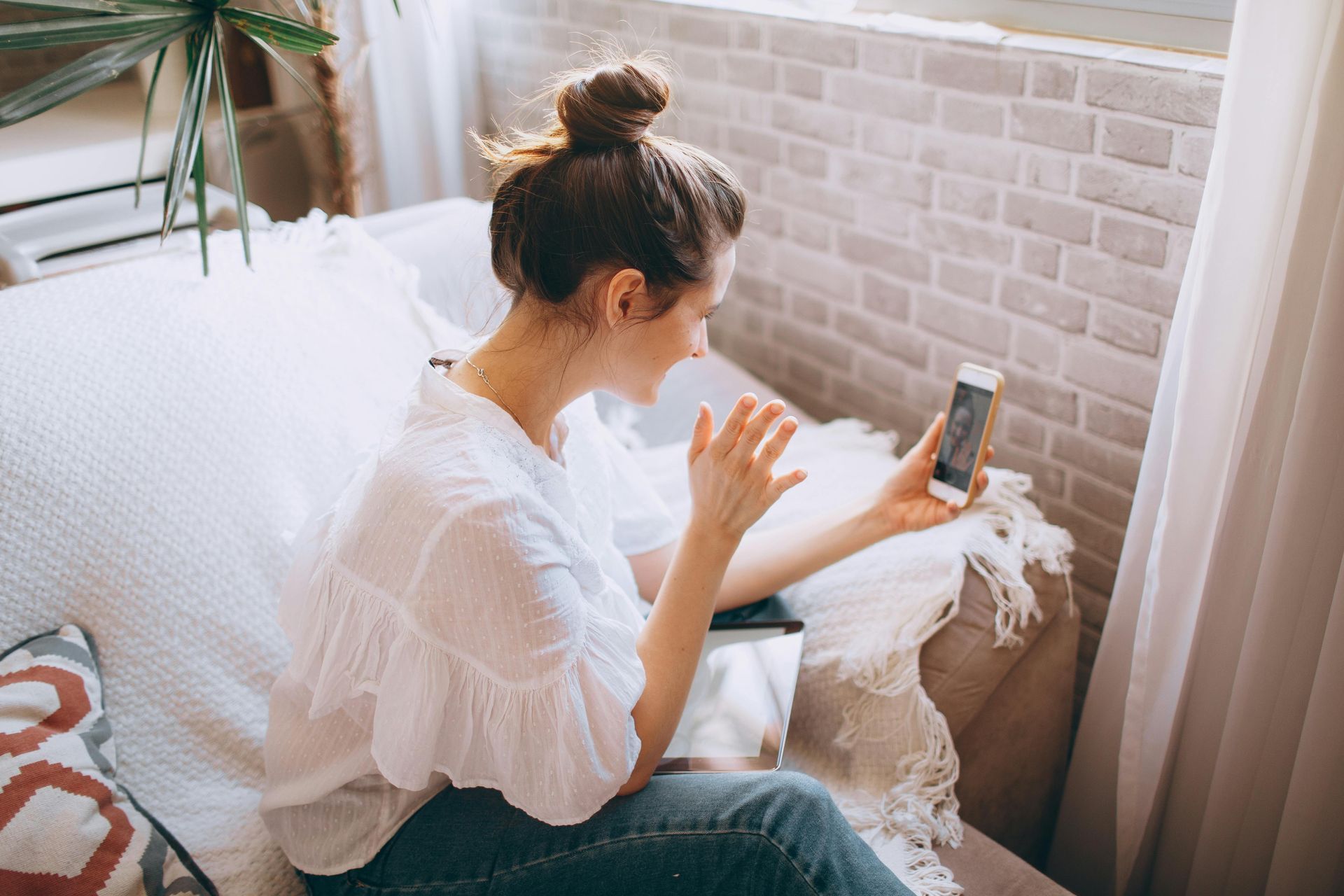 Woman on a couch video chatting on her phone in a bright room