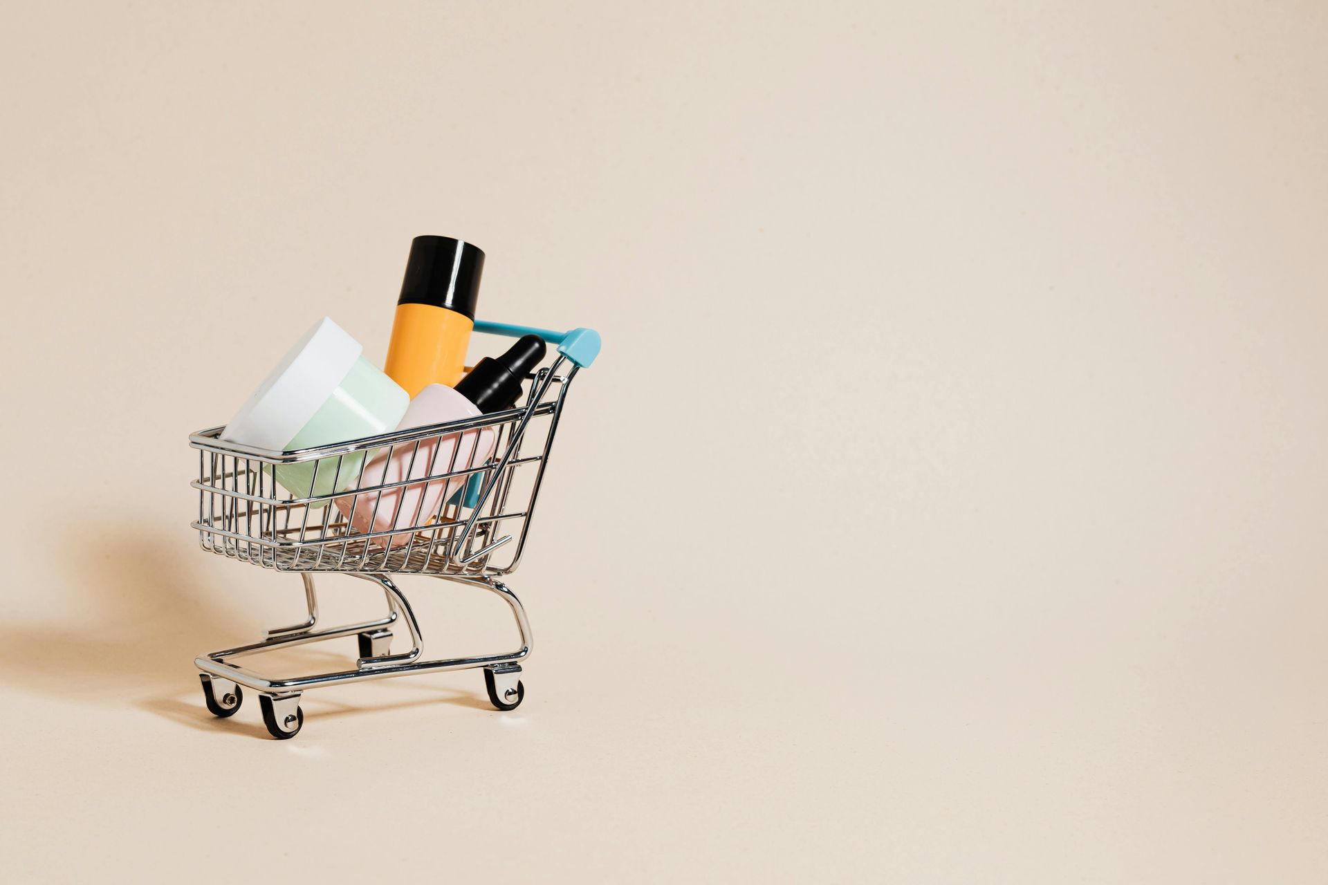 Mini shopping cart filled with assorted toiletries on a beige background