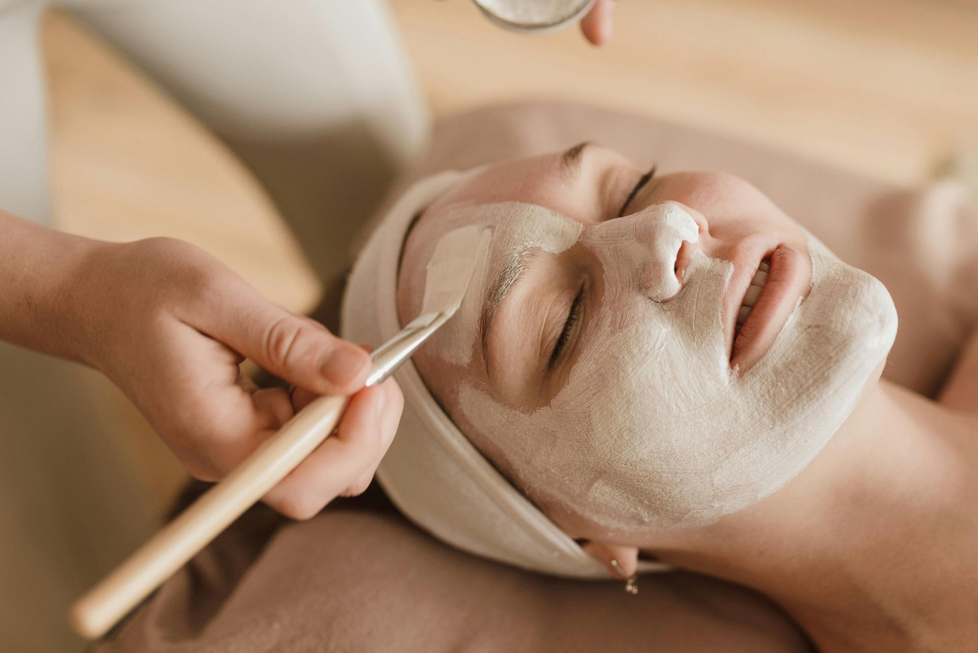 Woman receiving a facial massage with a rose quartz roller, wearing a beige towel headband and eyes closed