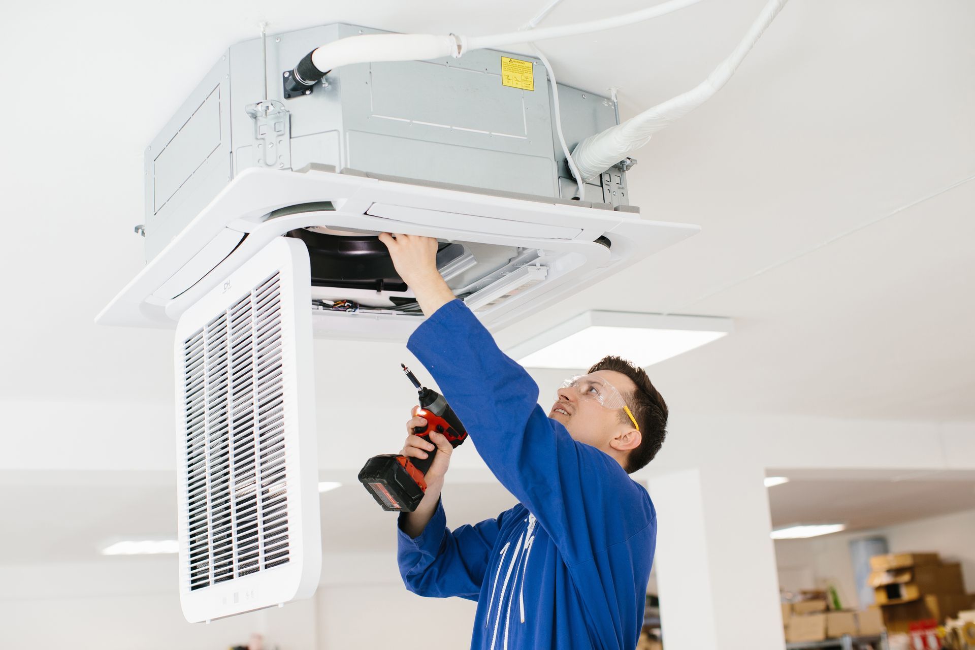 An HVAC technician inspecting and adjusting a ceiling-mounted industrial air conditioning.