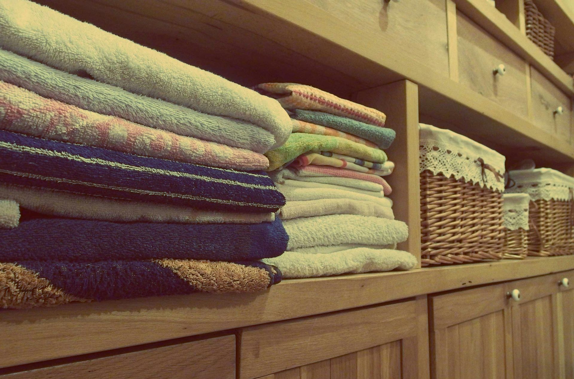 Shelves with folded towels and woven baskets in a wooden cabinet.