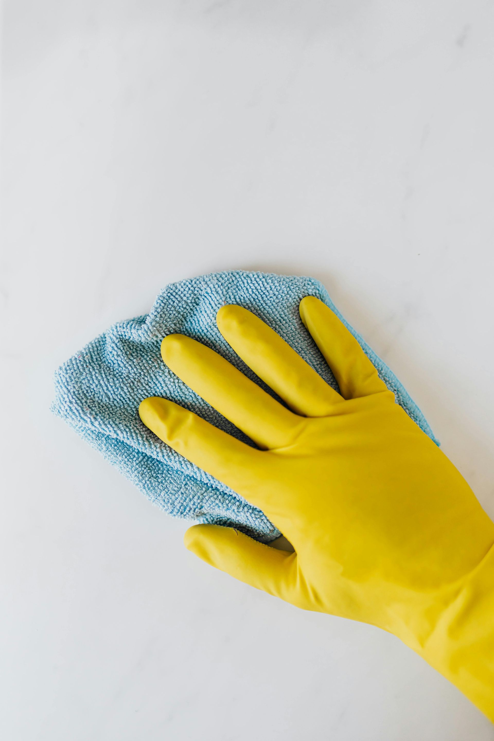 Yellow-gloved hand wiping a white surface with a blue cloth.