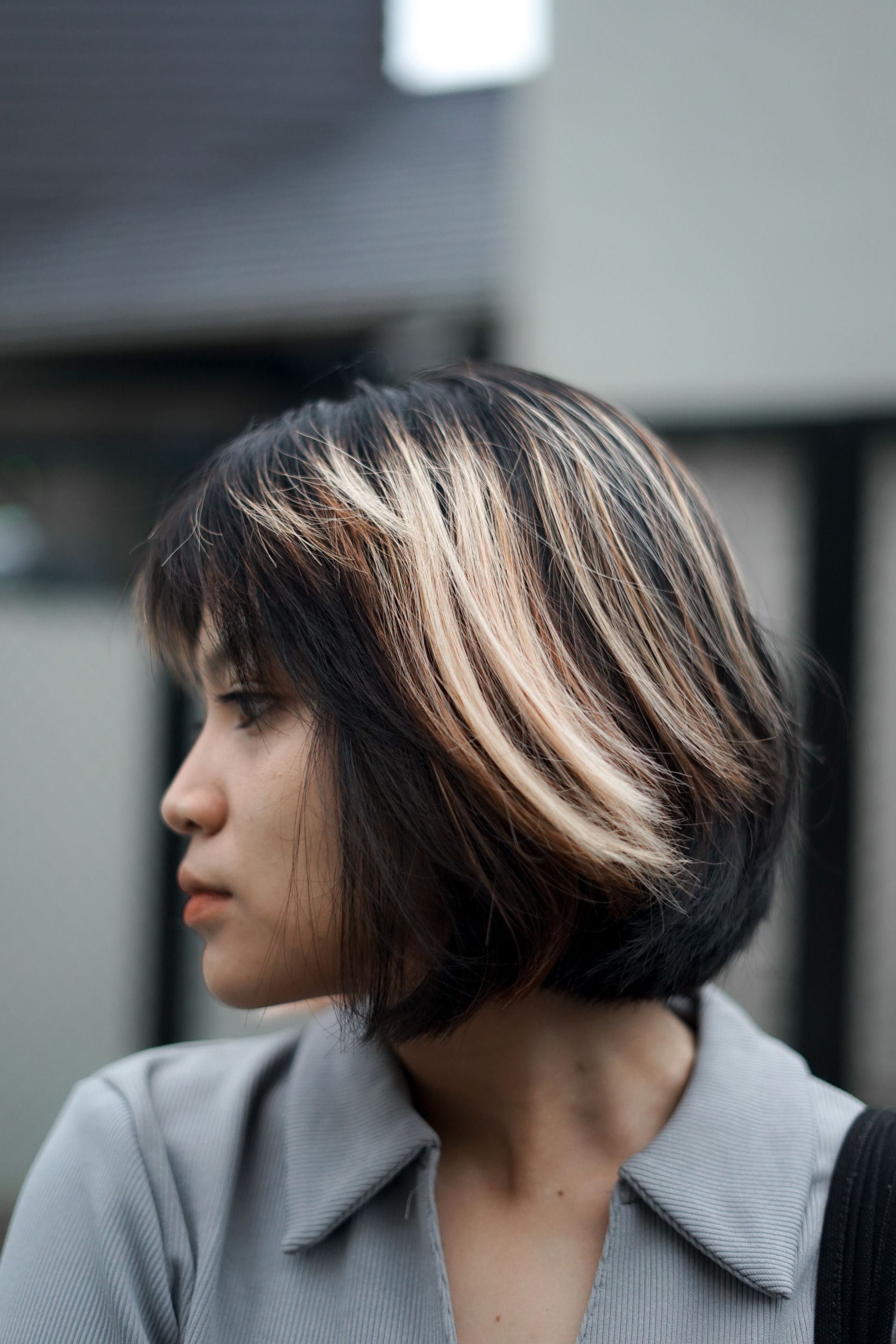Side profile of a person with a short bob haircut wearing a gray collared jacket outdoors