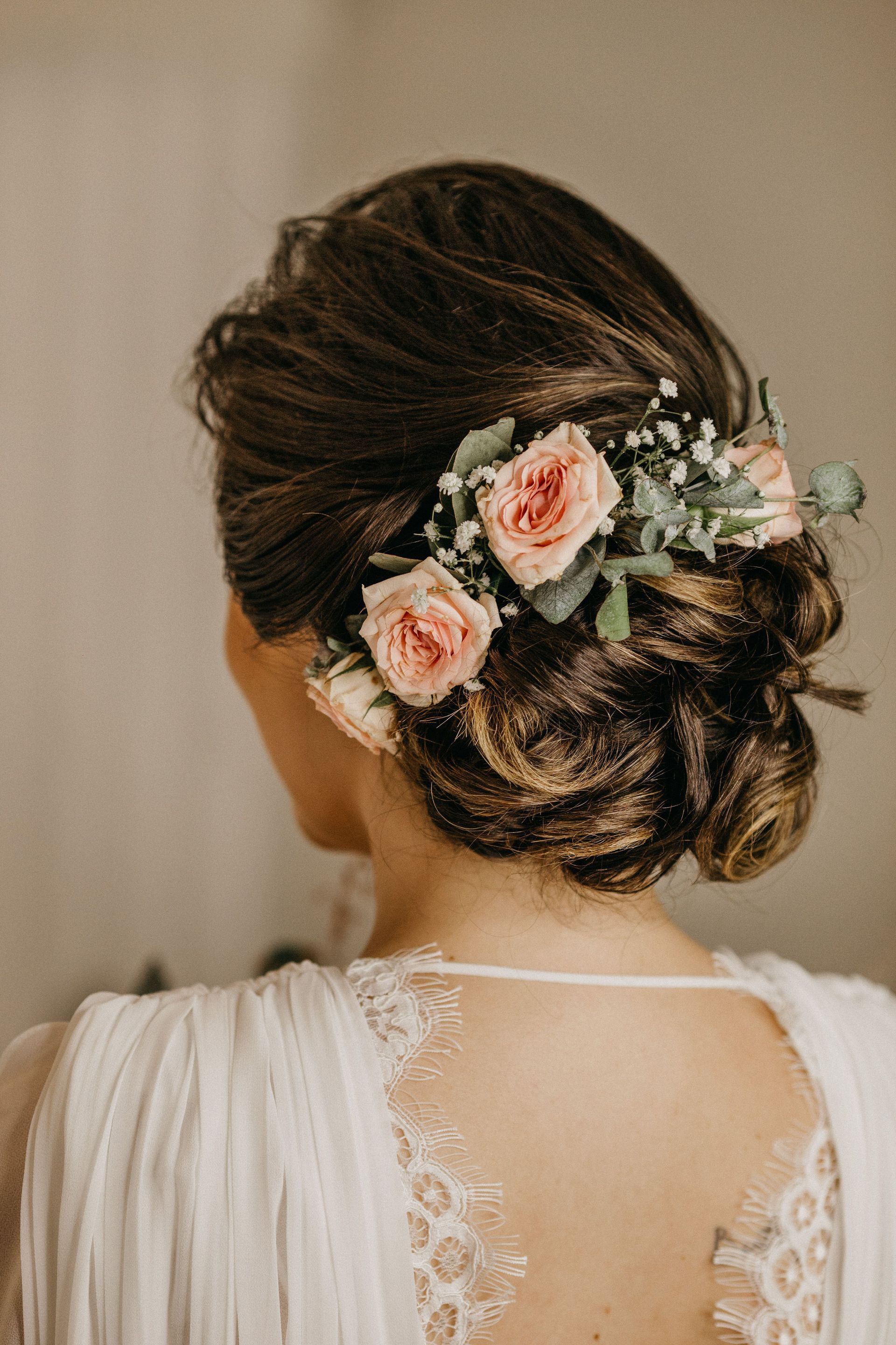 Bride with floral hairpiece in an elegant updo, seen from behind in a white lace dress