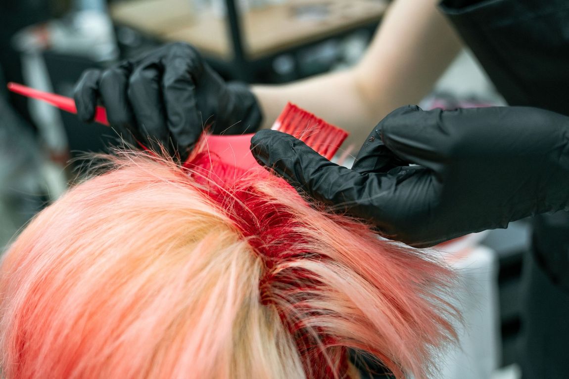 Hairdresser applying dark dye to short hair with brush and gloves in a salon