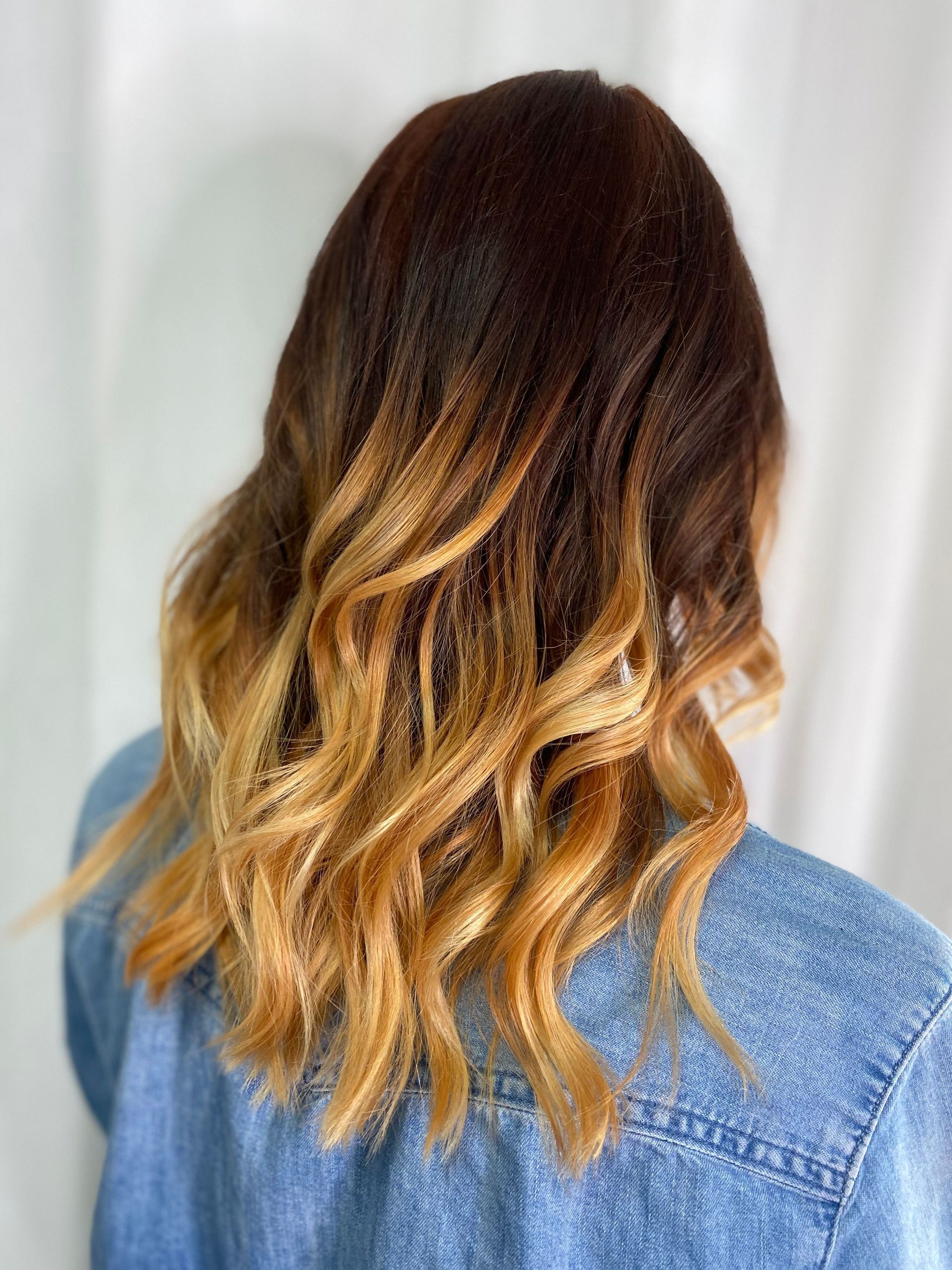 Wavy brown-to-blonde ombré hair shown from the back over a blue denim jacket