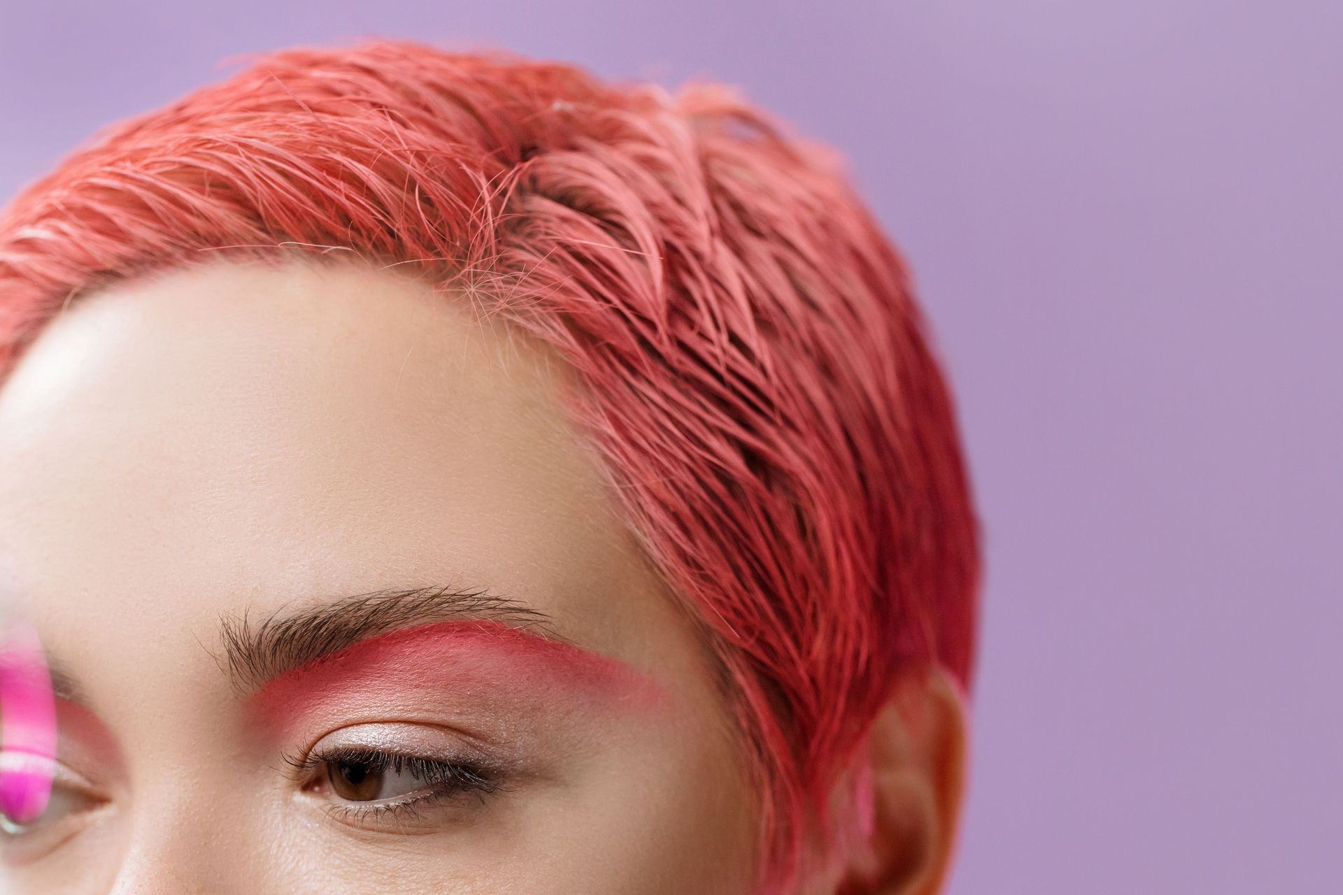 Close-up of a person with short pink hair and pink eyeshadow against a soft lavender background