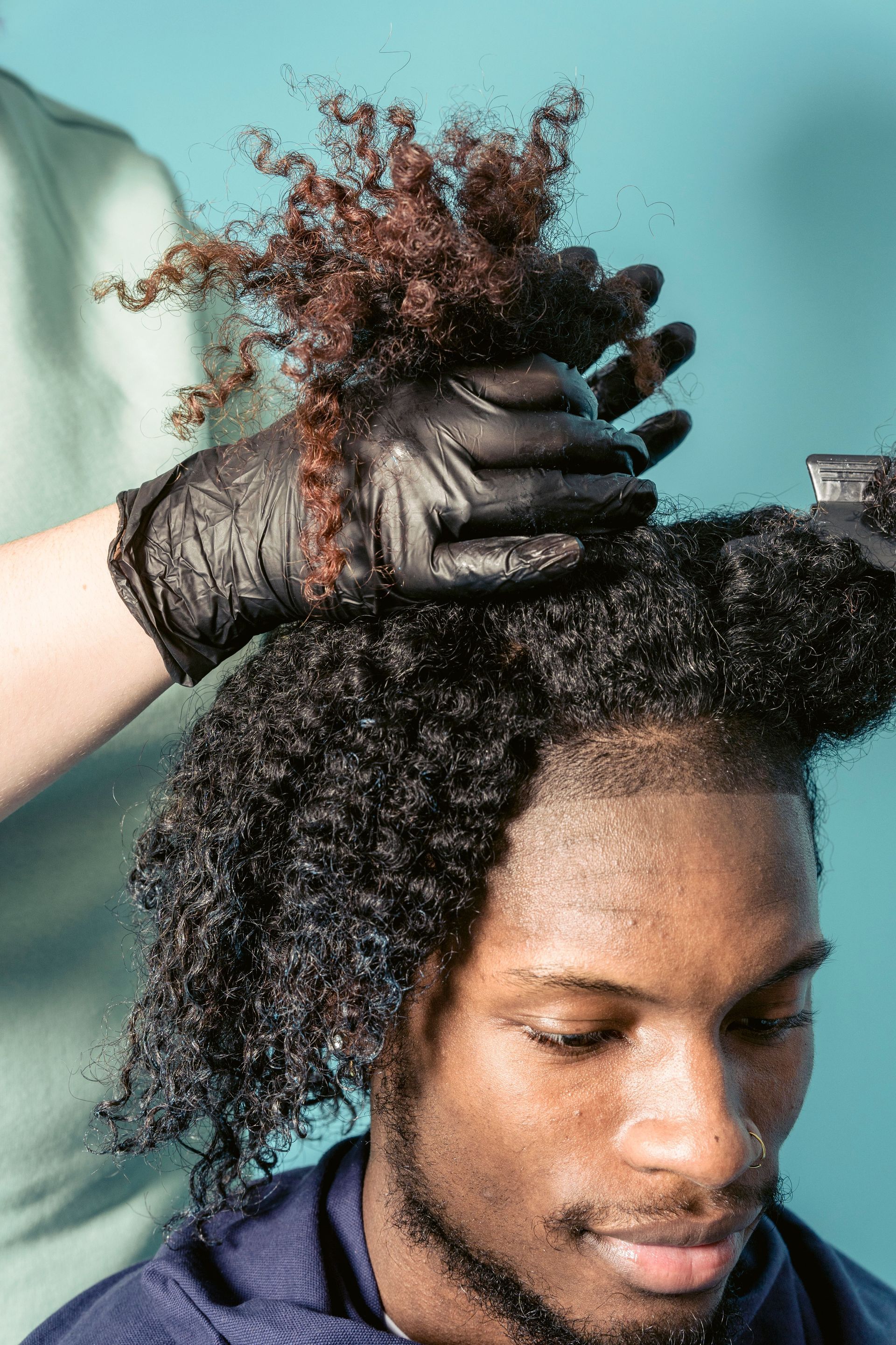Gloved hands styling curly hair against a teal background
