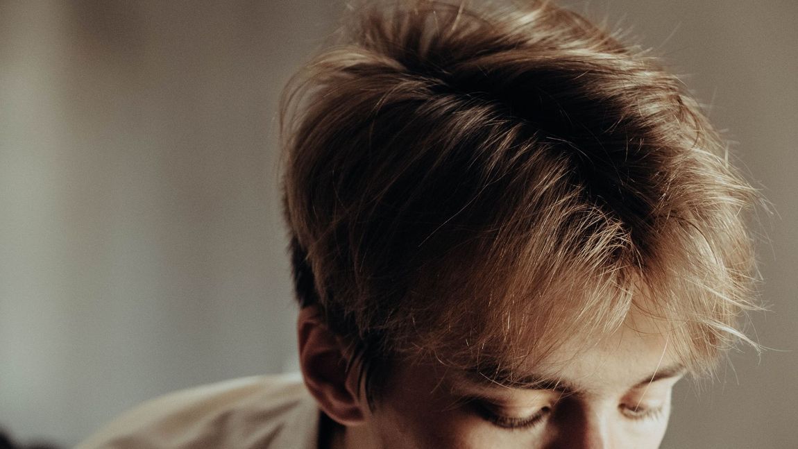 Close-up of a person with tousled brown hair looking downward against a blurred background