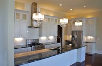 White kitchen with stainless steel appliances, dark countertops, and crystal chandeliers.