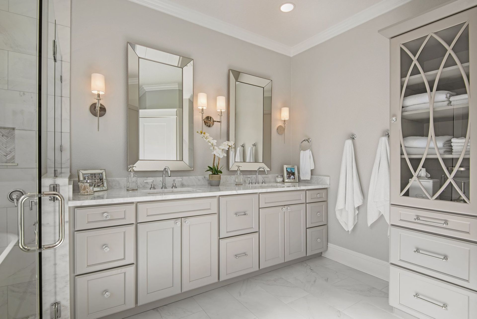 Bathroom with double vanity, two mirrors, and a linen cabinet. Soft gray cabinets, marble countertops, white walls.
