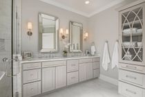 Bathroom with double vanity, large mirrors, built-in storage, and white marble accents.