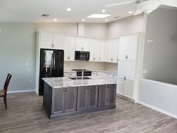 Kitchen with white and gray cabinets, island with sink, black refrigerator, and wood-look flooring.