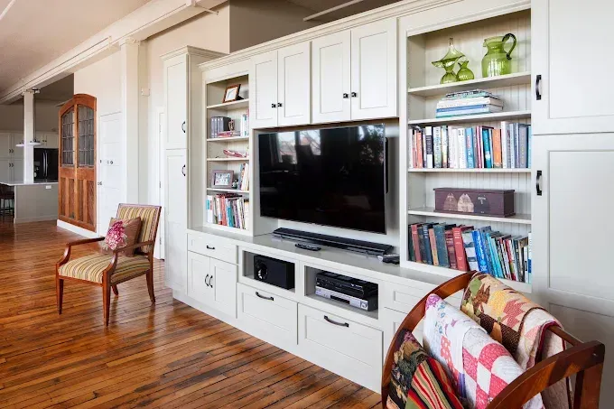 Built-in white cabinets with a TV, shelving, and storage in a room with hardwood floors.