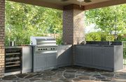 Outdoor kitchen with built-in grill, sink, and wine cooler on a stone patio, under a covered patio space.